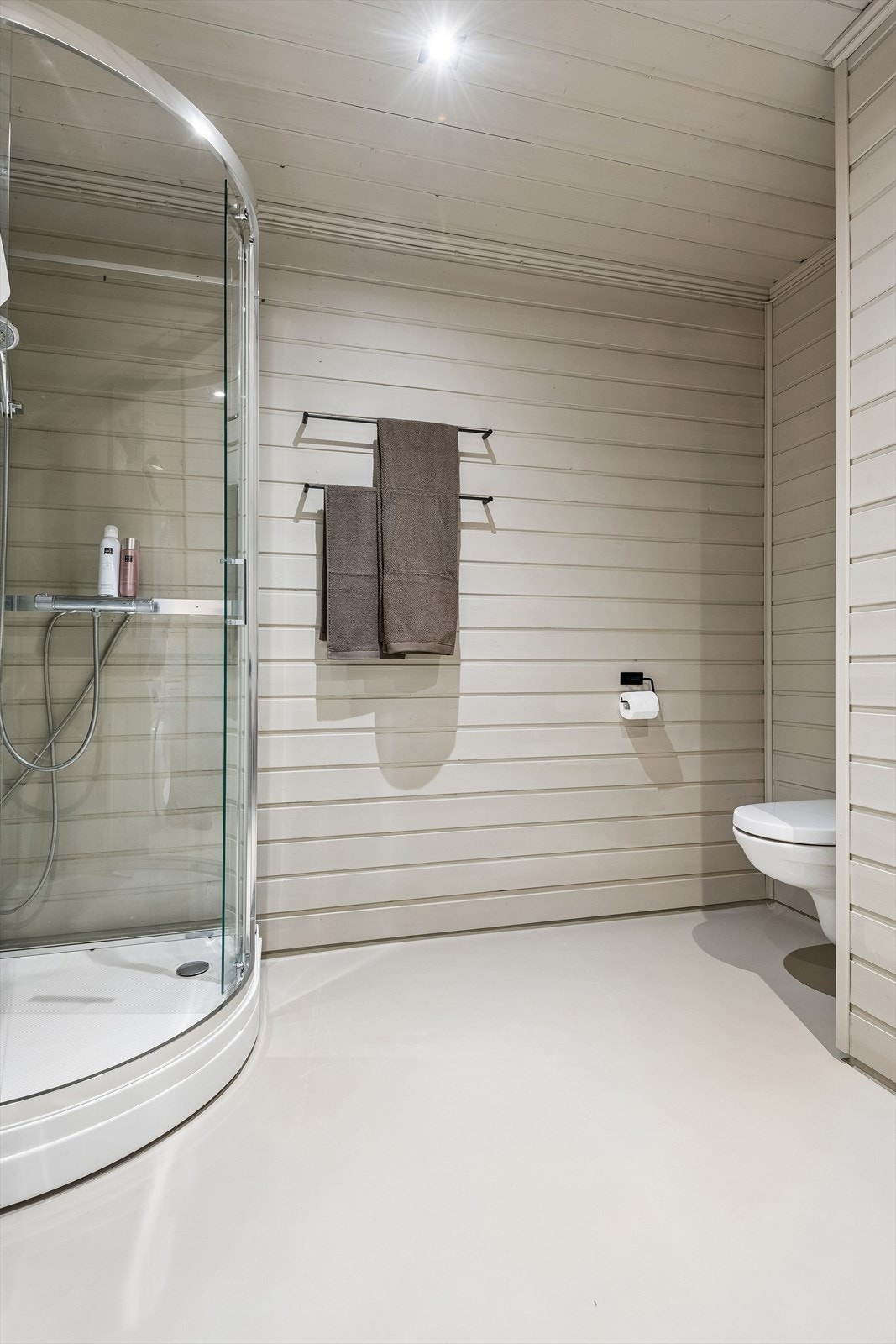 Badet har belegg på gulvet, panel på veggene, dusjkabinett og vegghengt toalett. Galleribilde