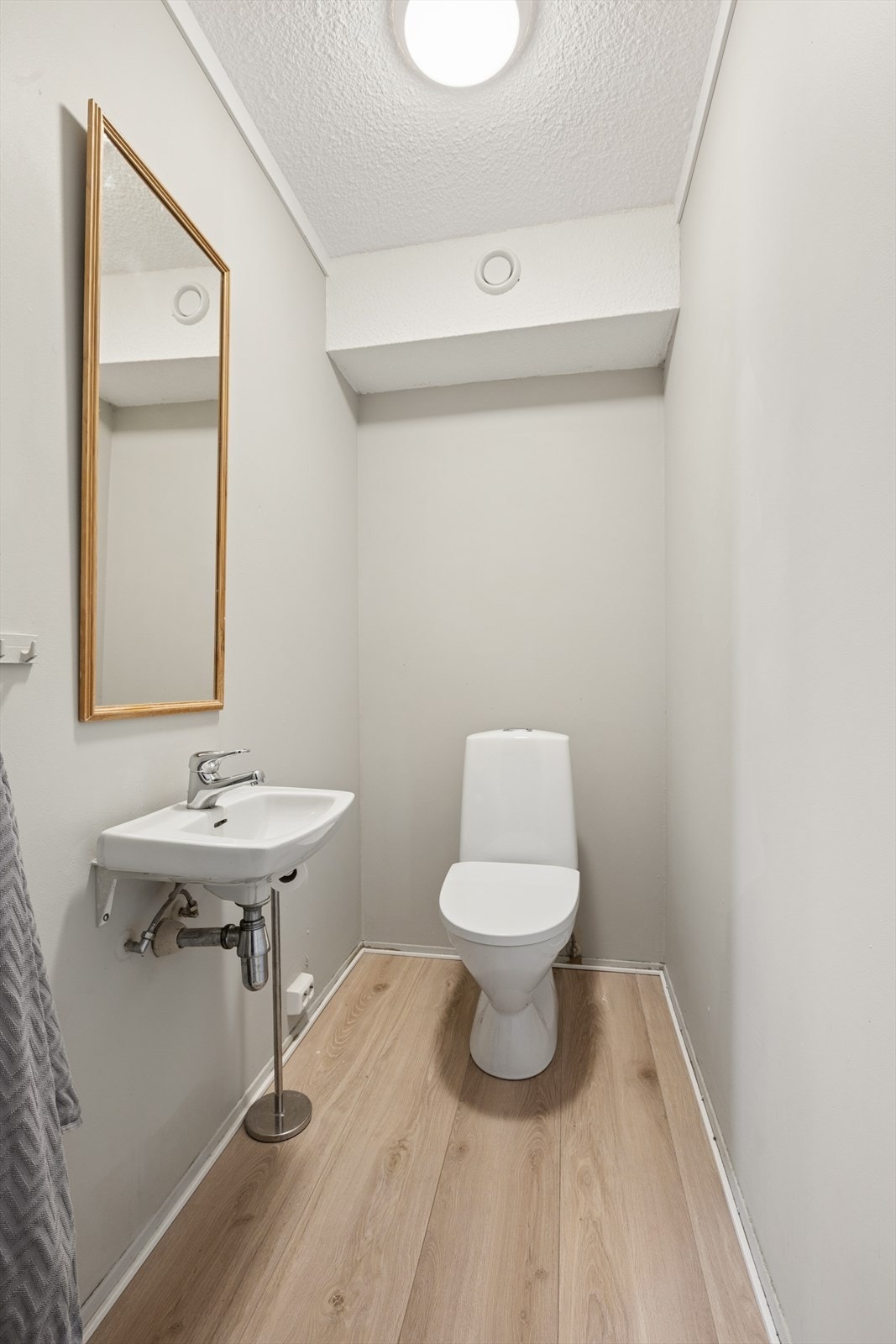 På boligens WC er det slette vegger, med et frittstående toalett, og vegghengt servant. Galleribilde