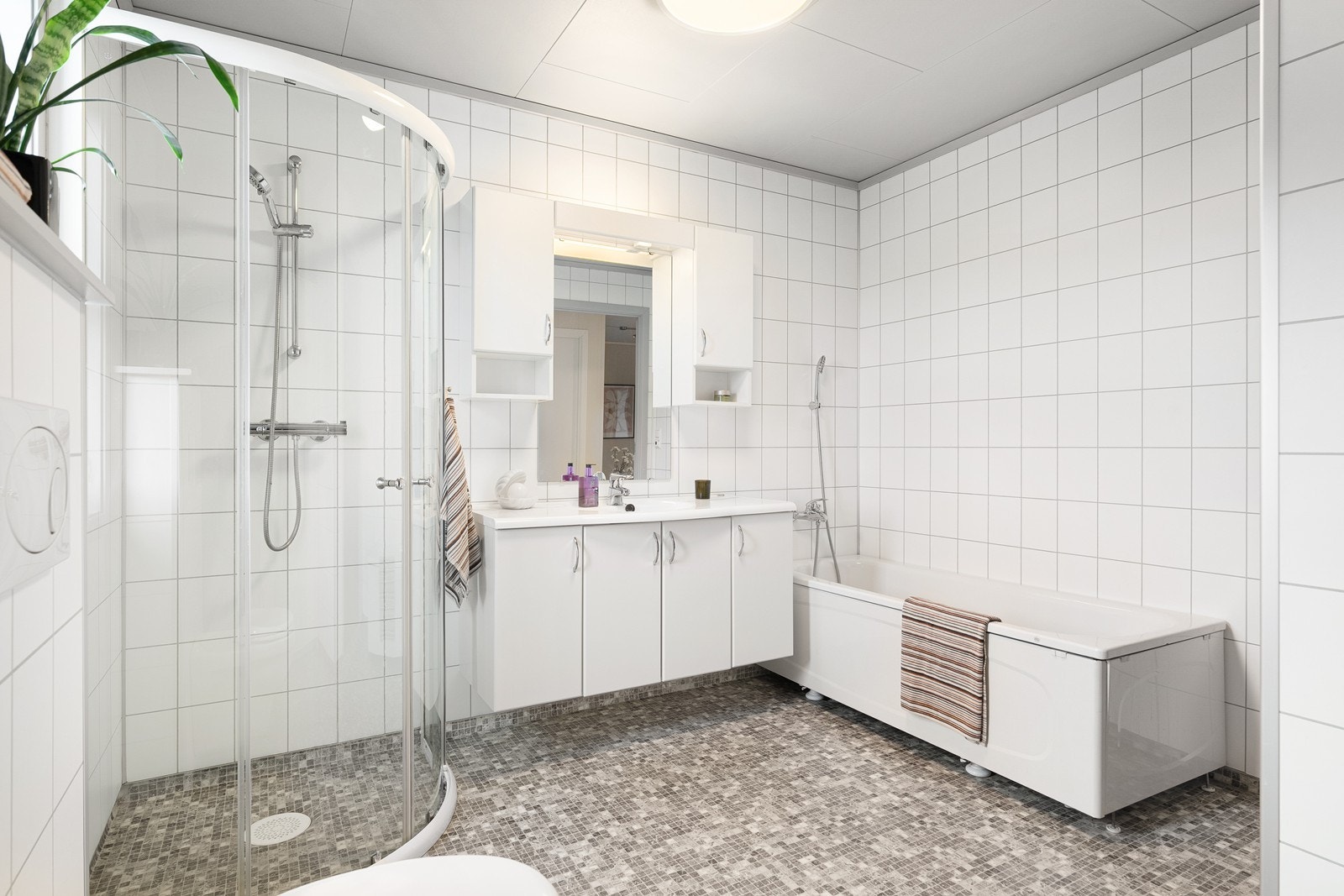 Badet har både dusjhjørne og badekar, samt et vegghengt toalett som gir et ryddig inntrykk og letter rengjøringen. Det er opplegg for vaskemaskin, og varmekabler i gulvet. Galleribilde