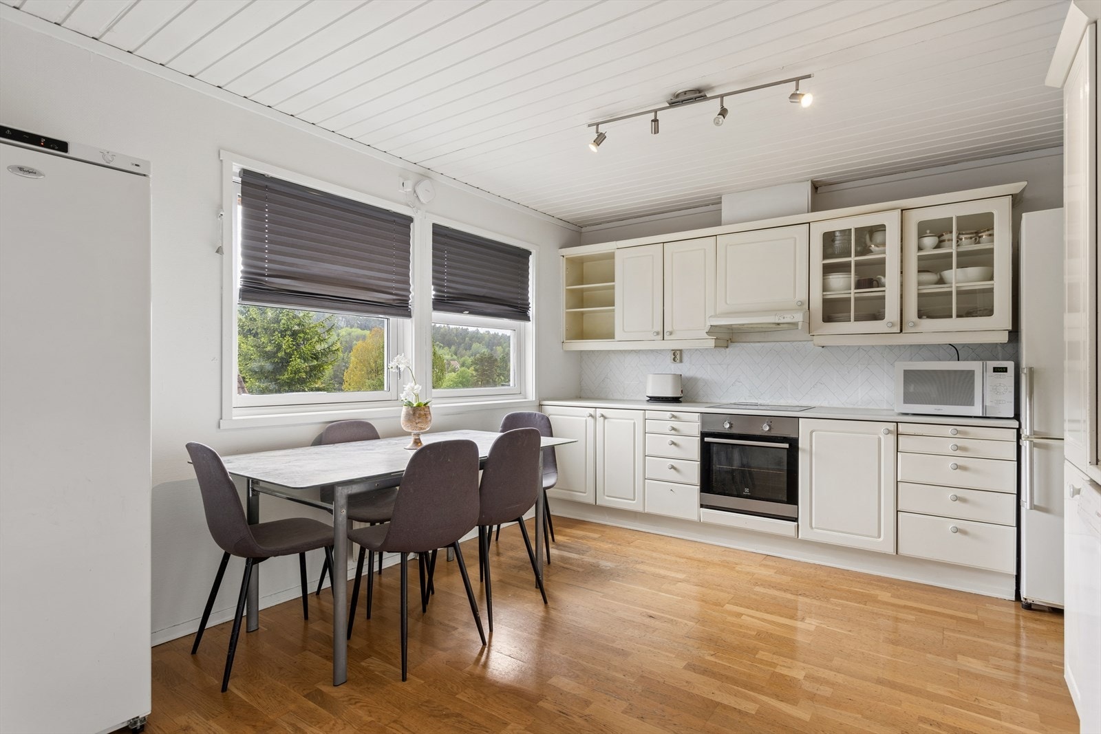 Kjøkken i eget rom med innredning med hvite, profilerte fronter, laminat benkeplate med nedfelt kum i rustfritt stål og ett-greps blandebatteri. Galleribilde