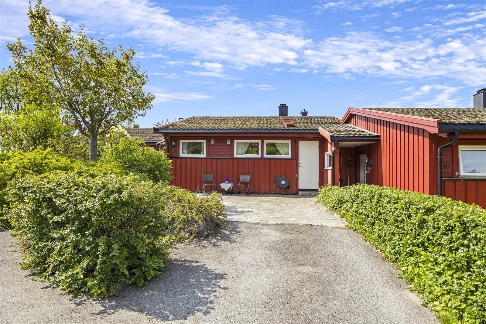 Asfaltert innkjørsel og skiferlagt terrasse ved inngangsparti. Bed og hekk mot gate. Galleribilde