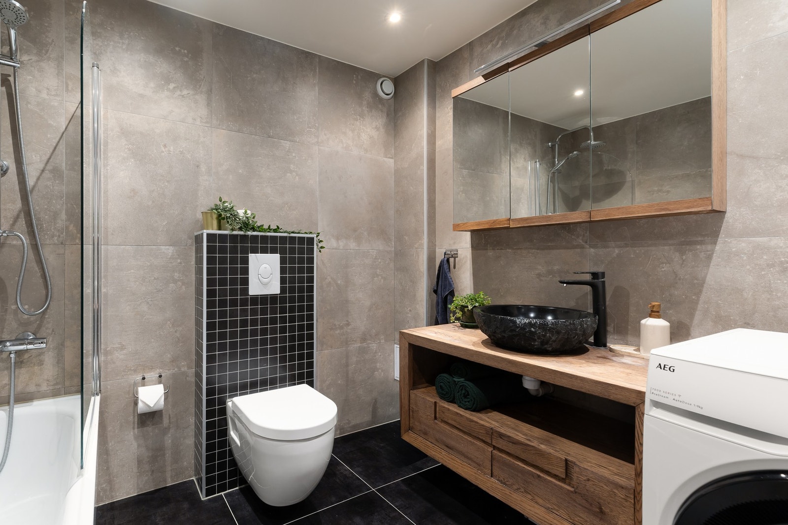 Videre har badet badekar med regnfallsdusj og opplegg for vaskmaskin/tørketrommel. Galleribilde