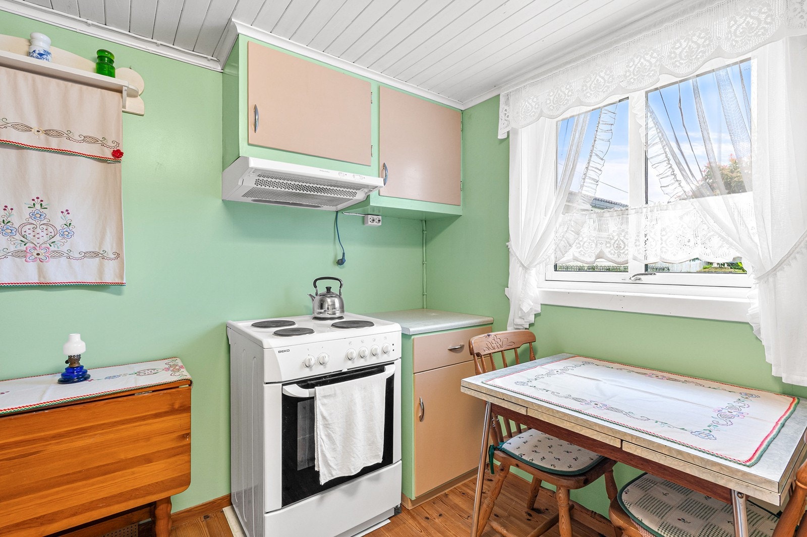 Det er tregulv på kjøkkenet og malte plater på veggene. Plass til spisebord ved vindu. Galleribilde