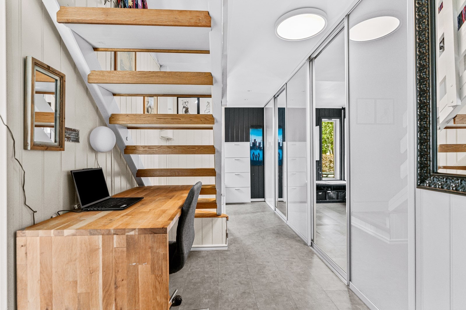 Gangen er innredet med en stor, plasstilpasset skyvedørsgarderobe som har fem dører med hvite fronter og speil. Under trappen er det fin plass til en kontorløsning eller lignende. Galleribilde