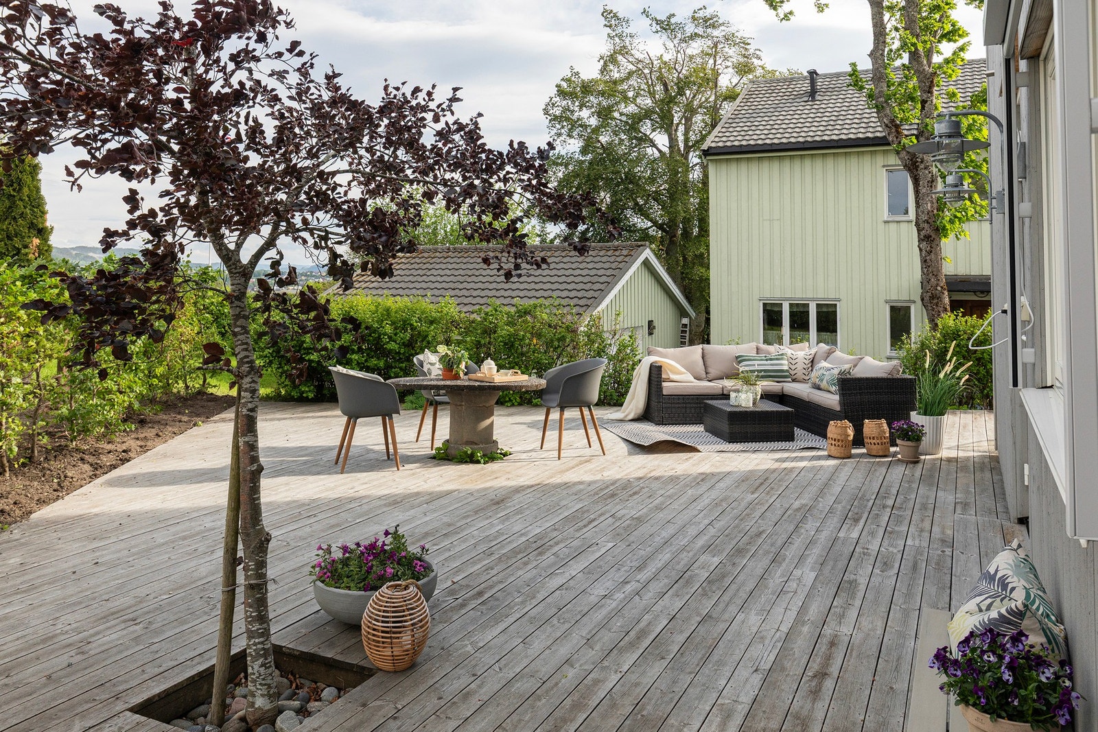 Hyggelige og frodige omgivelser på terrassen. Denne er dessuten pent "innrammet" med en hekk mot nærmeste naboeiendom. Her kan man virkelig nyte sommerhalvåret. Galleribilde