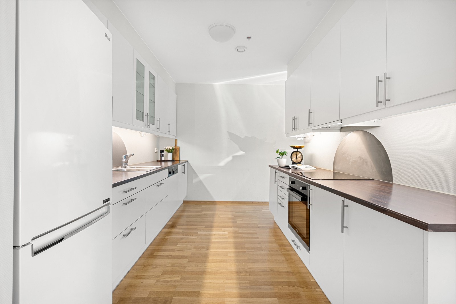 Tidsriktig kjøkken i hvit utførelse med skap til tak og integrert komfyr, platetopp og oppvaskmaskin gir et stilrent og funksjonelt uttrykk. Galleribilde