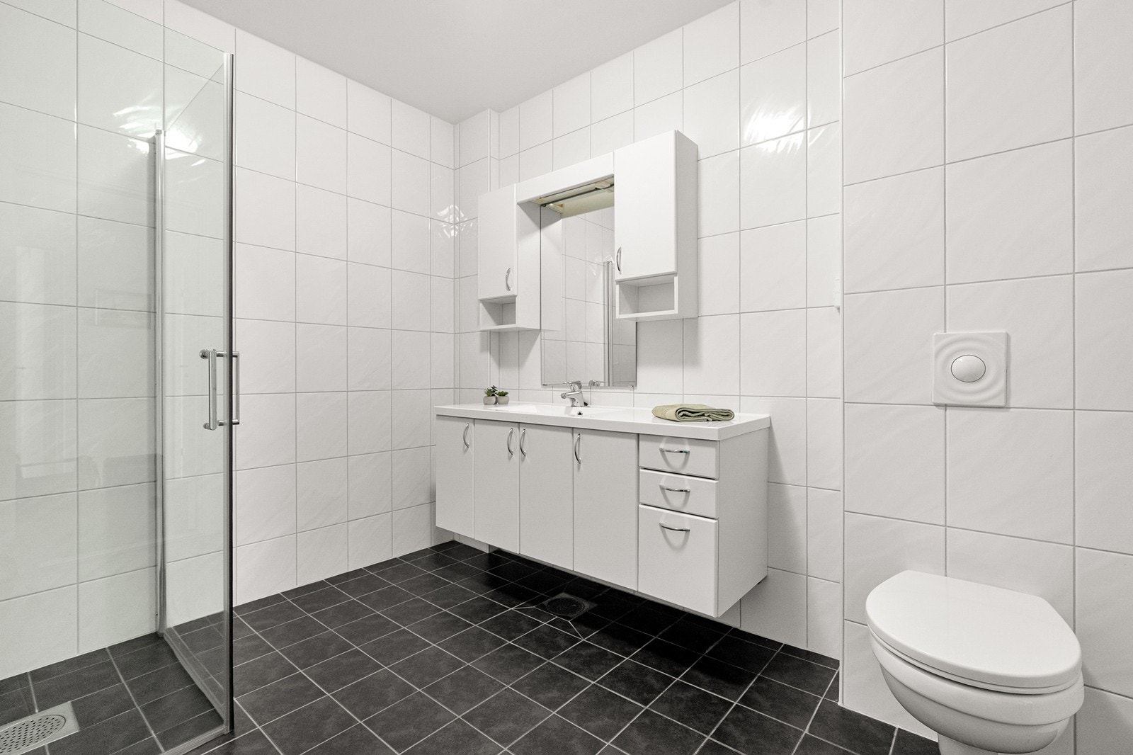 Badet er praktisk innredet med servant med nedfelt vask, veggmontert toalett og dusjhjørne med innfellbare dusjdører. Galleribilde