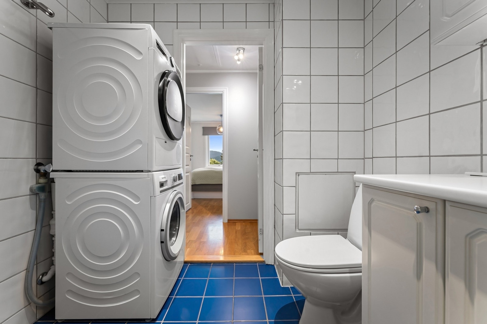 Badet har toalett, vegghengt servantinnredning, speil med overlys, dusjhjørne med dører og opplegg for vaskemaskin Galleribilde