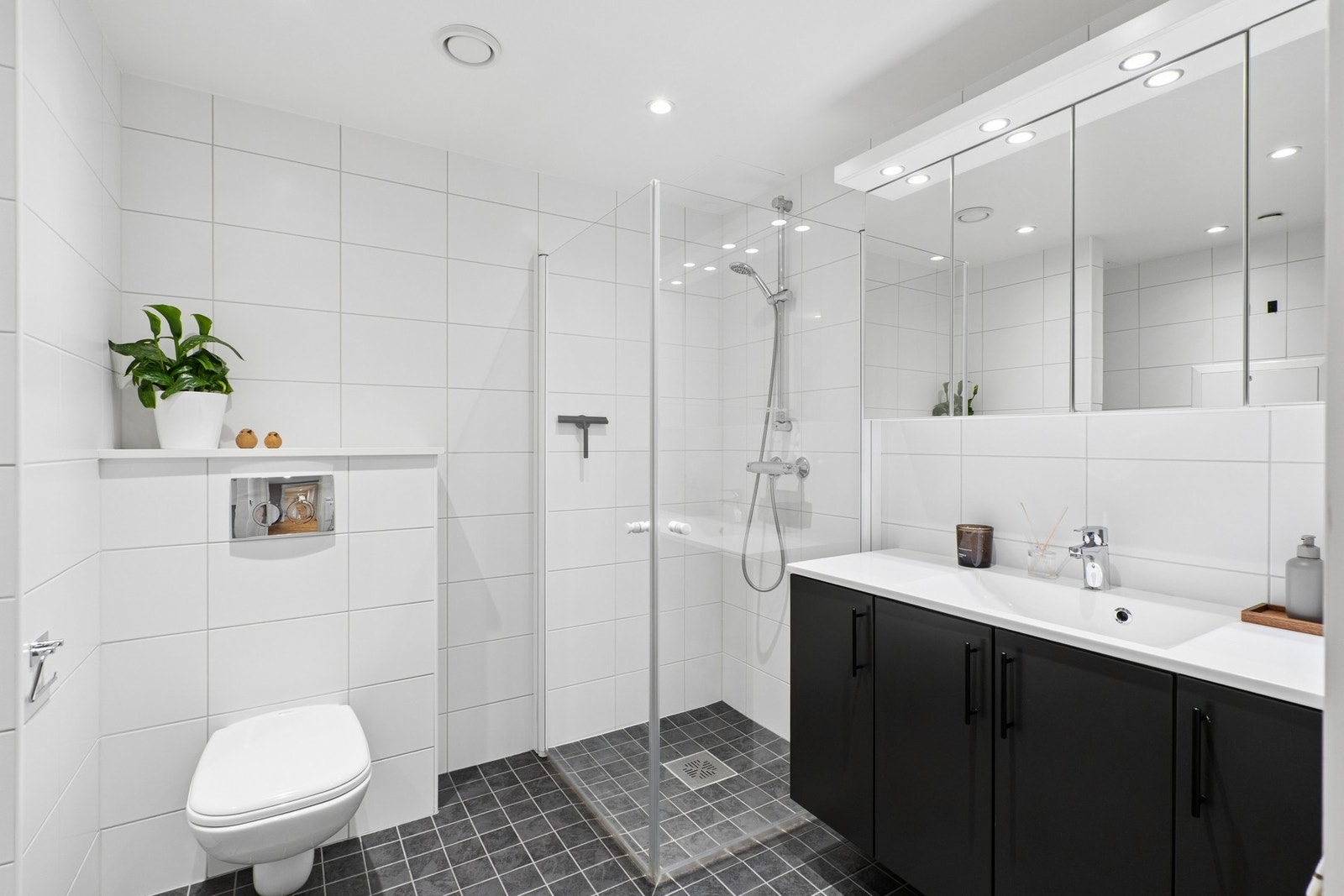 Badet er utstyrt med et dusjhjørne med innfellbare glassdører og et vegghengt toalett. Galleribilde
