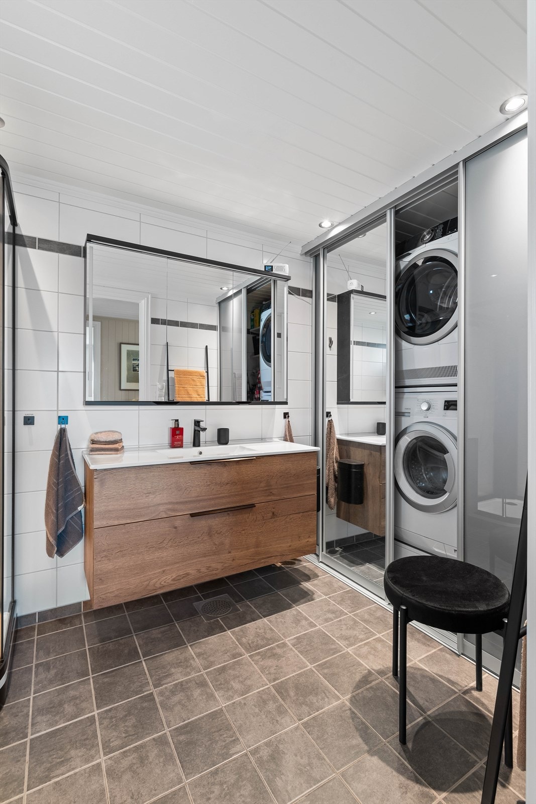 En spesielt smart detalj er vaskeromsnisjen; opplegg for vaskemaskin og tørketrommel er elegant skjult bak skyvedører. Dette gir badet et ryddig og rent uttrykk når maskinene ikke er i bruk. Galleribilde