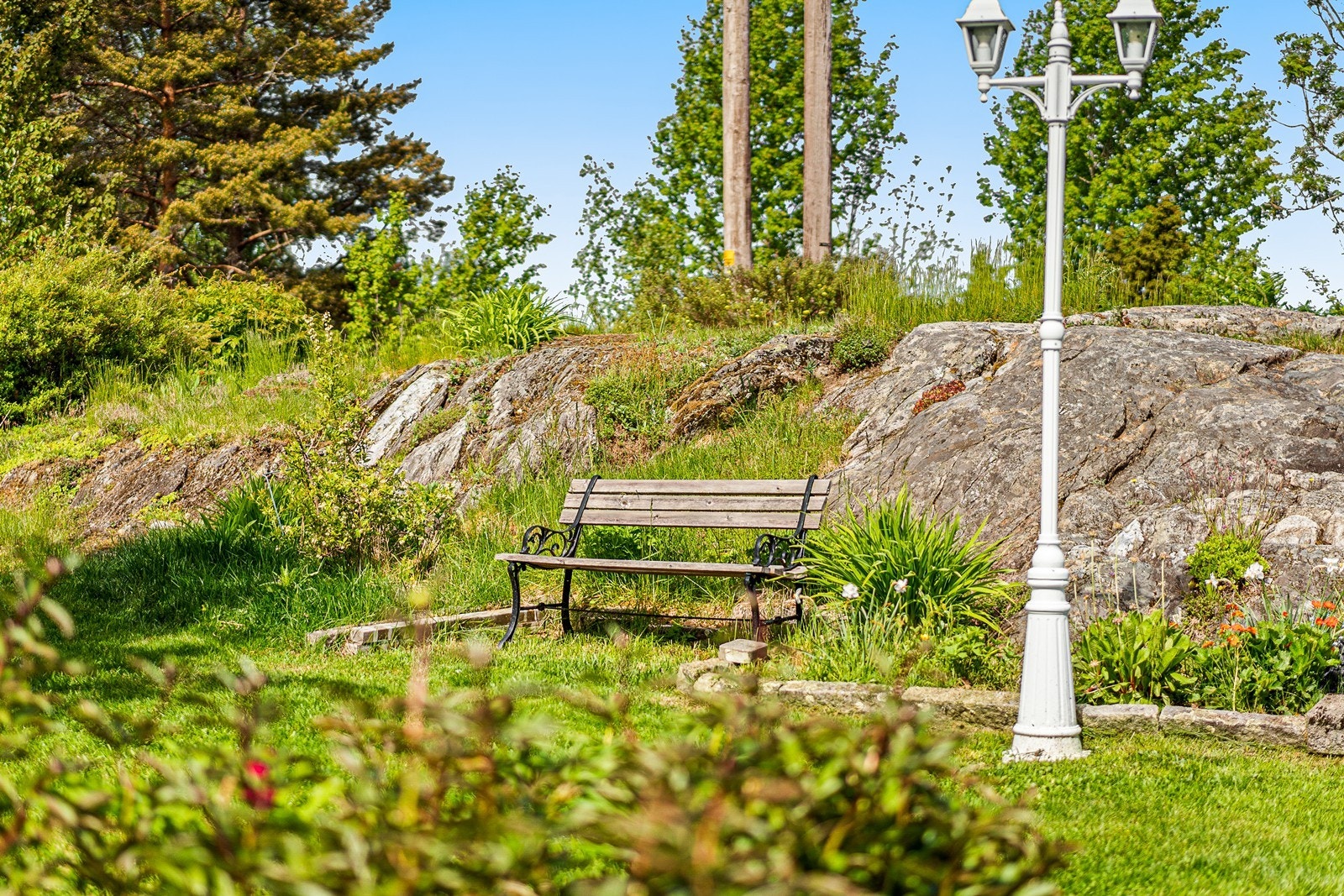 Naturlige berg, etablert beplantning og sittebenk skaper en sjarmerende atmosfære i hagen. Galleribilde