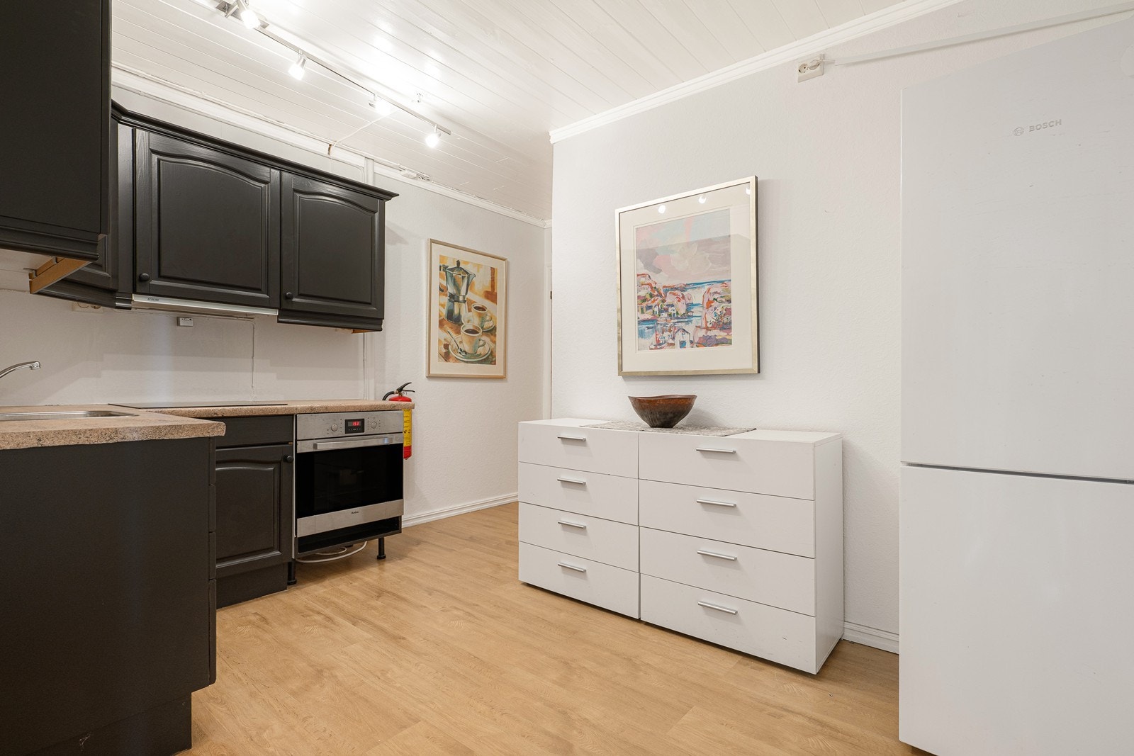 I tilknytning til kjellerstuen ligger det et kjøkken med sorte, profilerte fronter og beige laminatbenkeplate med nedfelt kum. Galleribilde