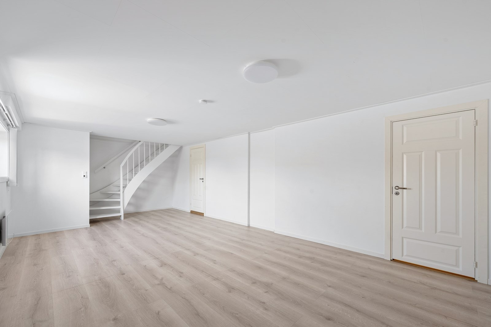 Romslig og innbydende kjellerstue med gode møbleringsmuligheter. Rommet holder en lys og nøytral fargepalett med malte overflater og laminatgulv, noe som gir et moderne og helhetlig uttrykk. Galleribilde