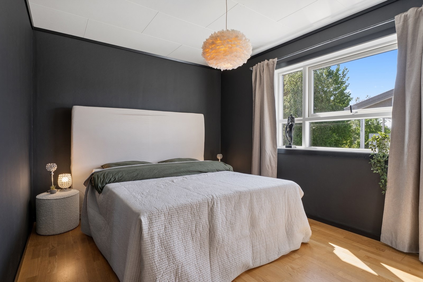 Soverommet har parkett på gulvet og malte veggflater og et stort vindu som inviterer lyset og fargene fra naturen inn. Galleribilde