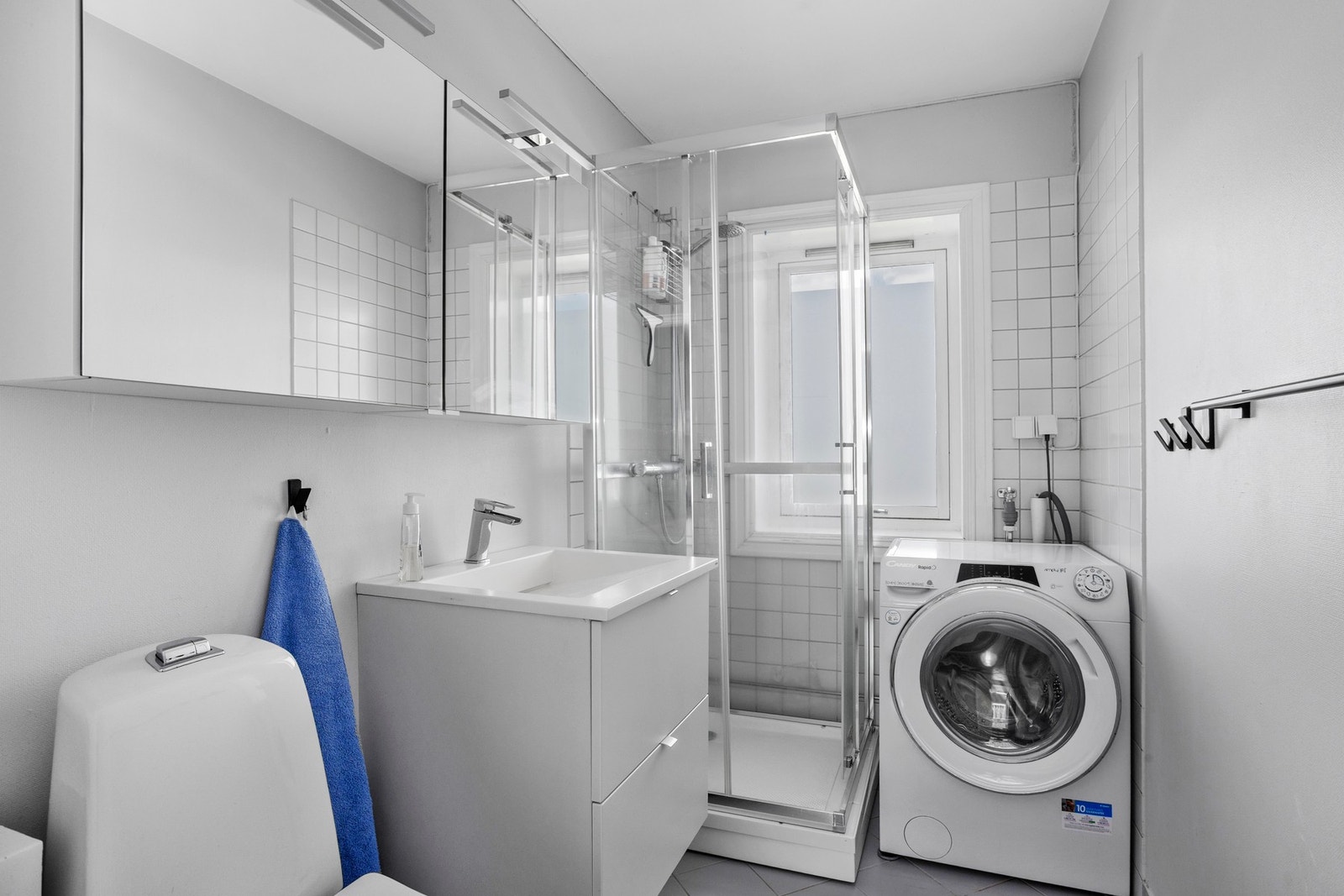 Badet har flislagt gulv med varmekabler, flislagte vegger med malt strie og sokkelflis, malt tak, dusjkabinett, toalett og opplegg for vaskemaskin Galleribilde