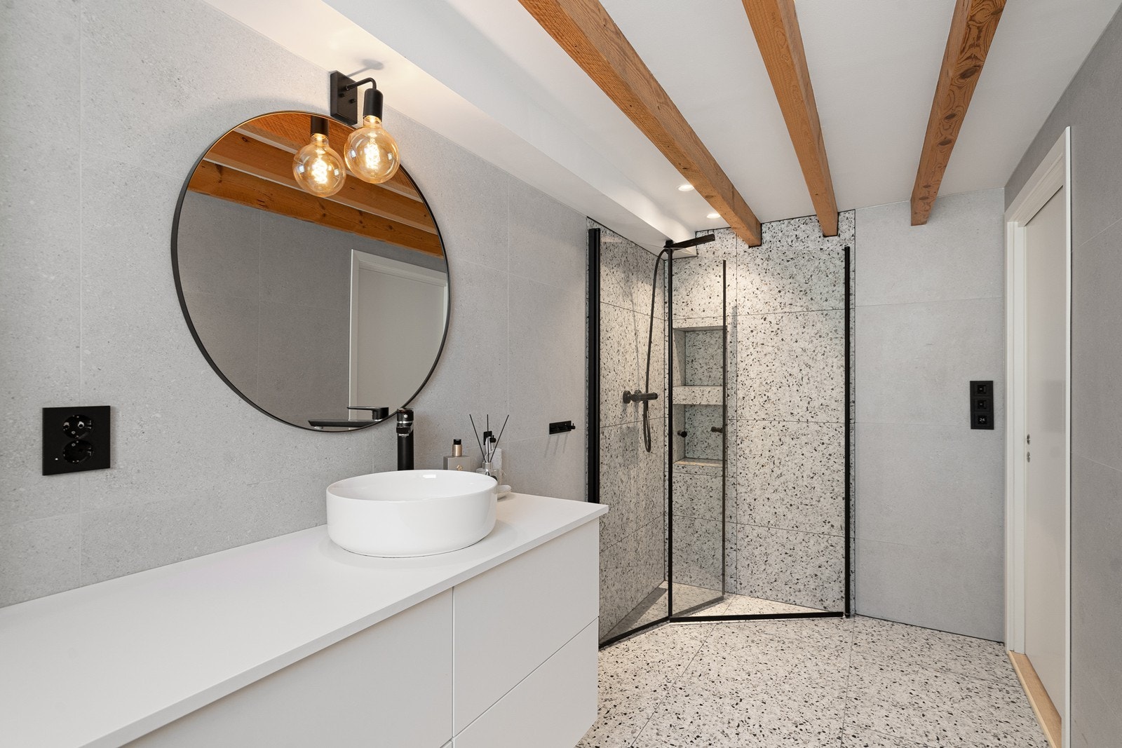 Badet har vegghengt toalett, moderne baderomsinnredning med servant, speil og belysning, samt en stilren dusj med sort dusjgarnityr. Galleribilde