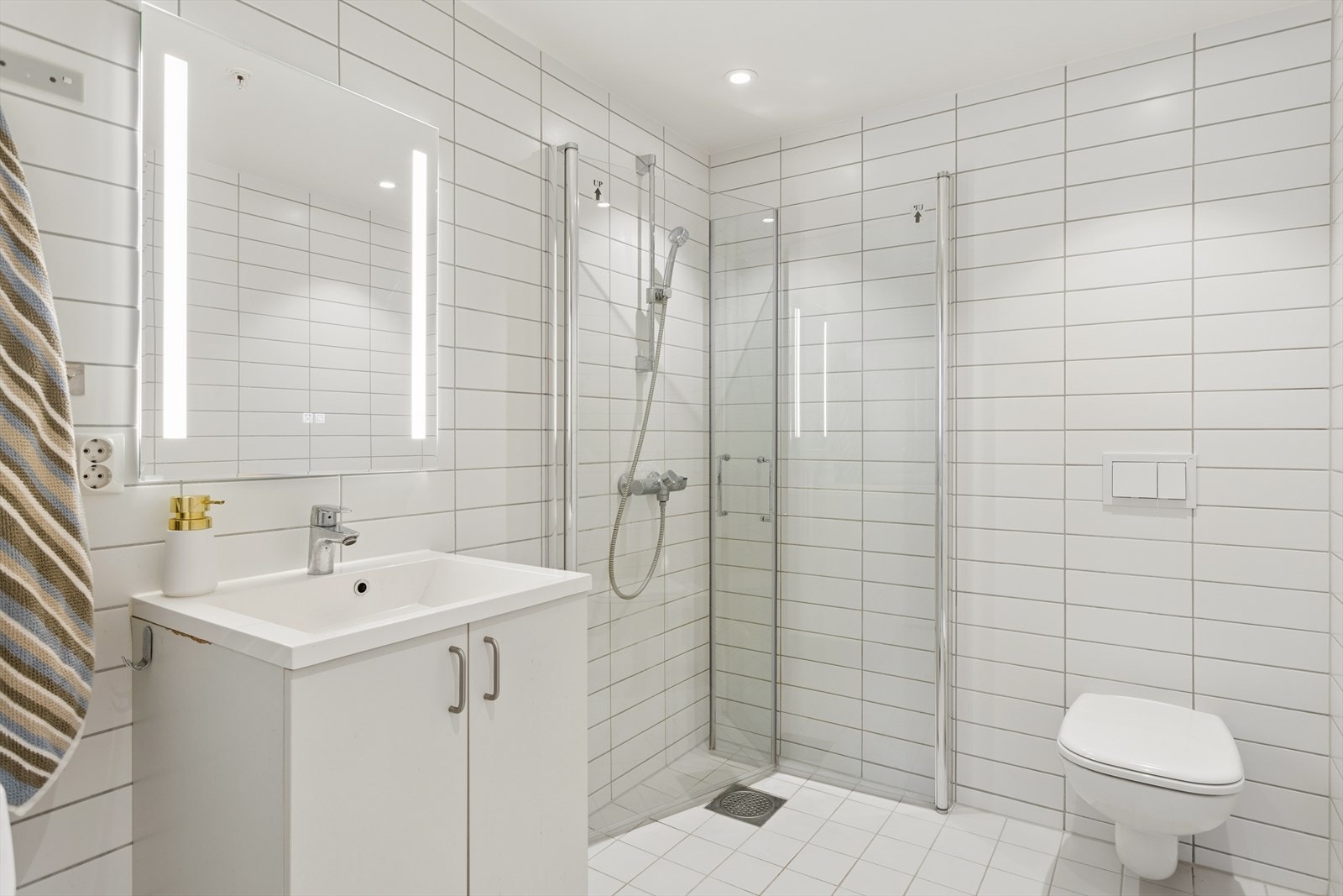 Lyst og moderne bad med flislagte overflater og en funksjonell planløsning. Badet er utstyrt med servantinnredning med nedfelt servant, vegghengt toalett og dusjhjørne med glassvegger. Galleribilde