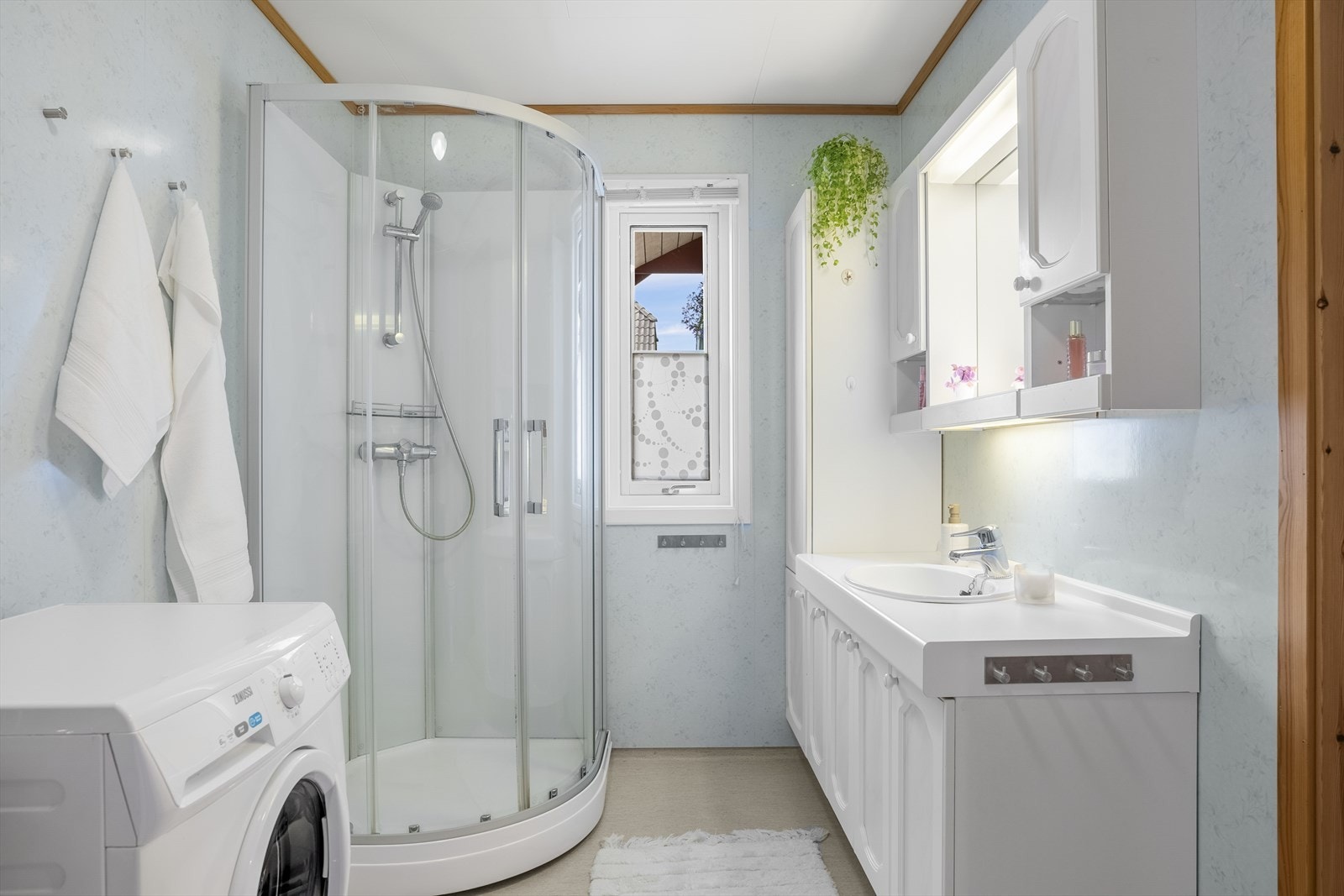 Badet er innredet med stor innredet servant, dusjkabinett, opplegg for vaskemaskin, varmtvannsbereder og utslagsvask. Galleribilde