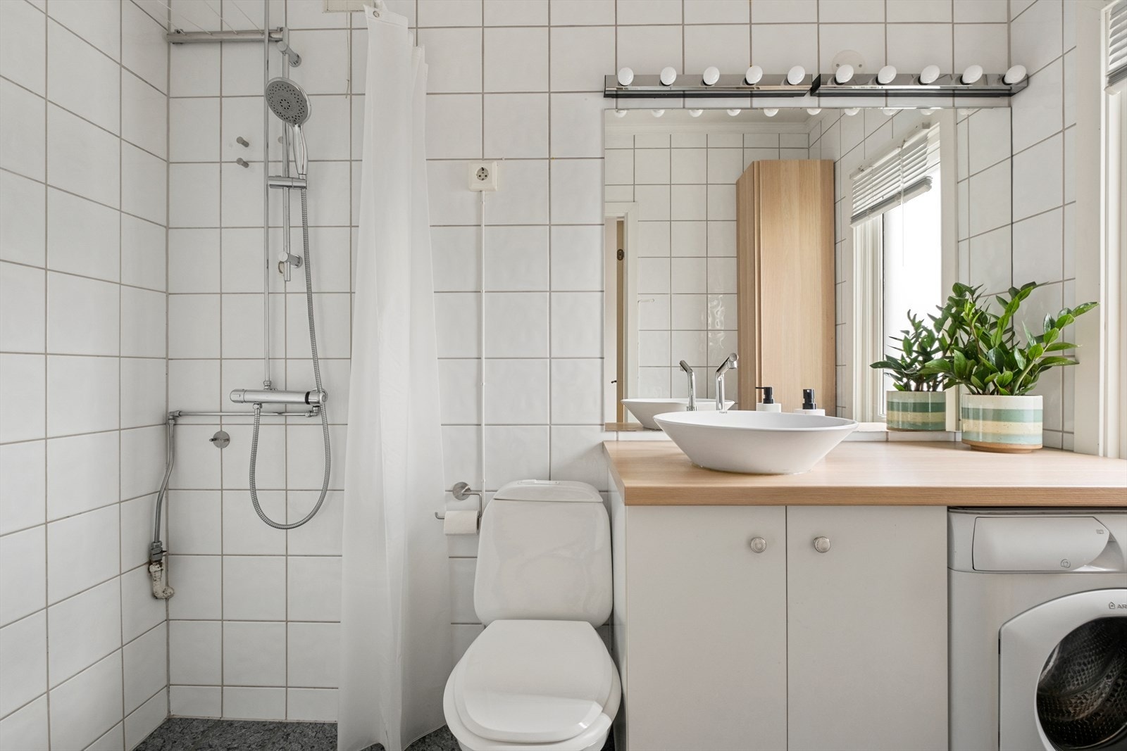 Badet er flislagt og utstyrt med dusj, servant med underskap, wc samt vaskemaskin. En arealeffektiv løsning på 3,4 kvm. Galleribilde