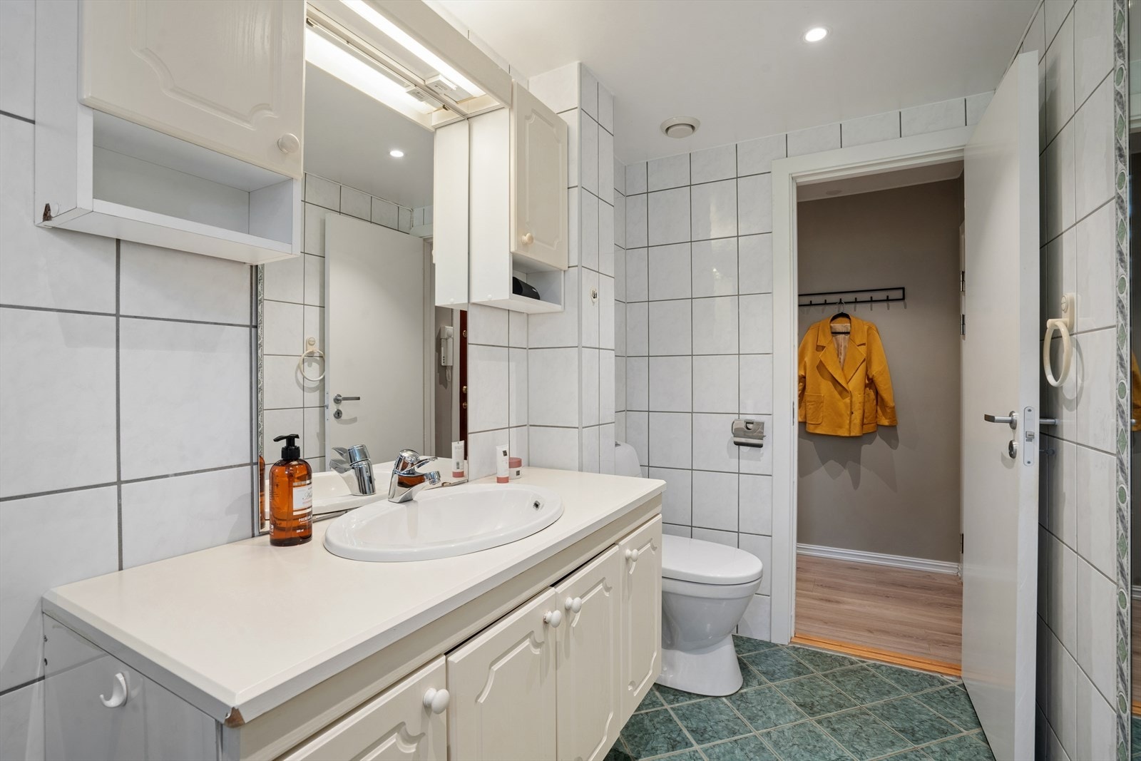 Her er det flislagte overflater med varmekabler i gulvet, gulvmontert toalett, speil og lysarmatur, samt nedsenket himling med malte plater og downlights. Galleribilde