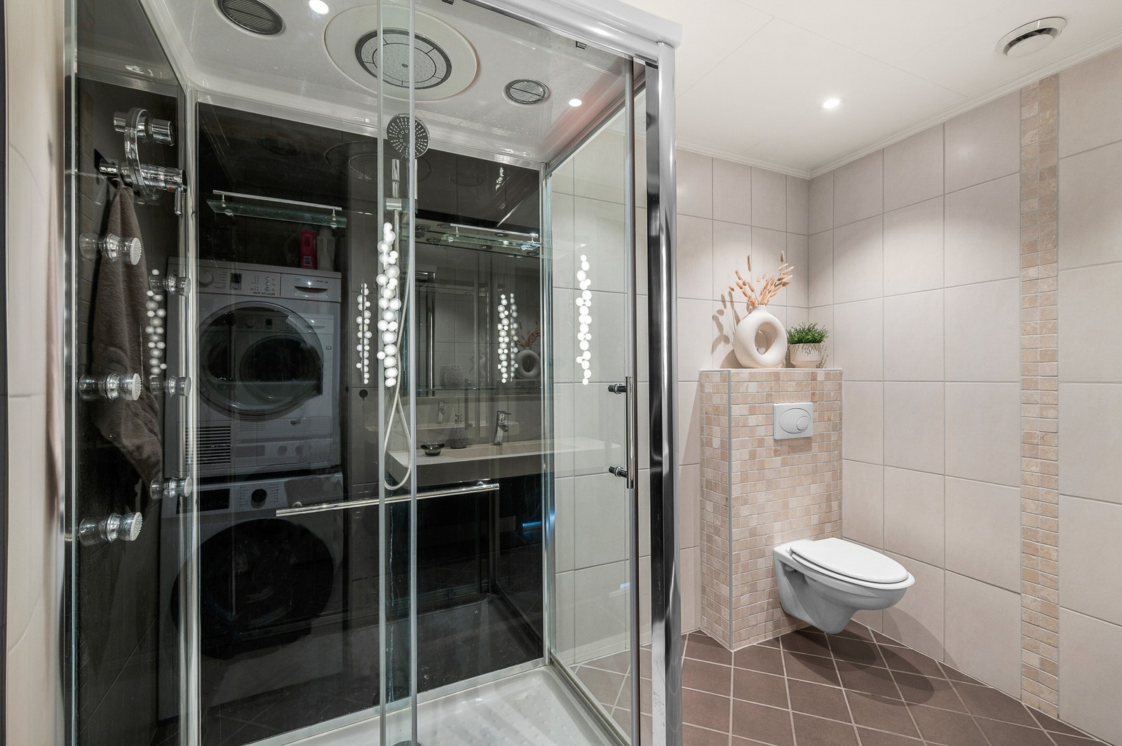 Badet er innredet med et stort servantskap, dusjkabinett, vegghengt toalett og opplegg for vaskemaskin og tørketrommel. Galleribilde
