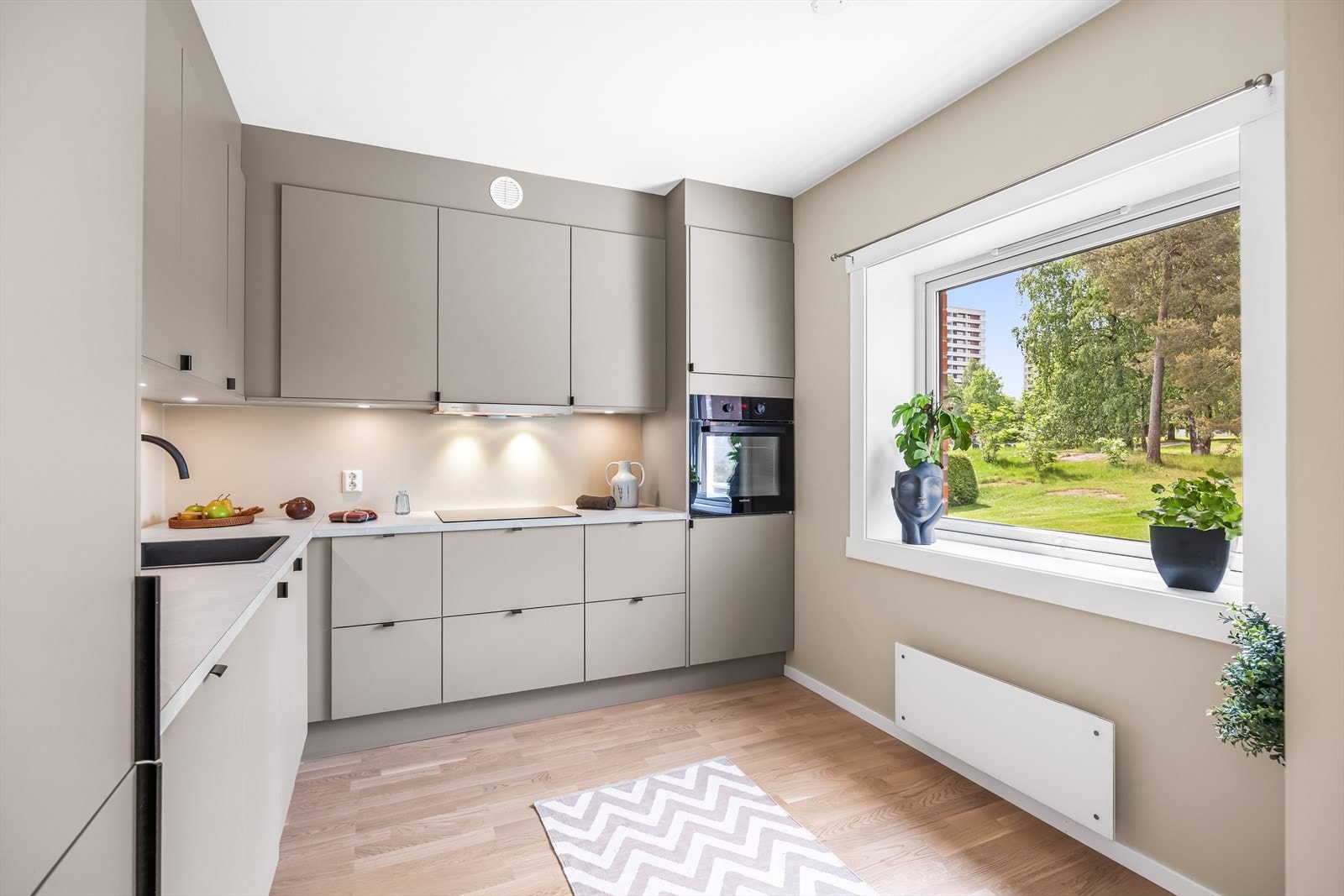 Lekkert HTH-kjøkkeninnredning med integrerte hvitevarer. Det er plass til en spiseplass ved vinduet. Galleribilde