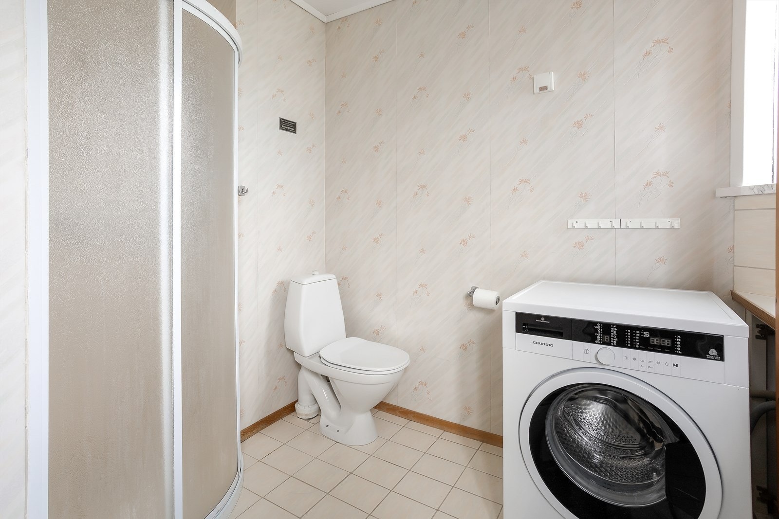 Badet har fliser på gulv, samt fliser og tapet på veggene. Rommet er innredet med dusjvegger og gulvstående toalett. Galleribilde