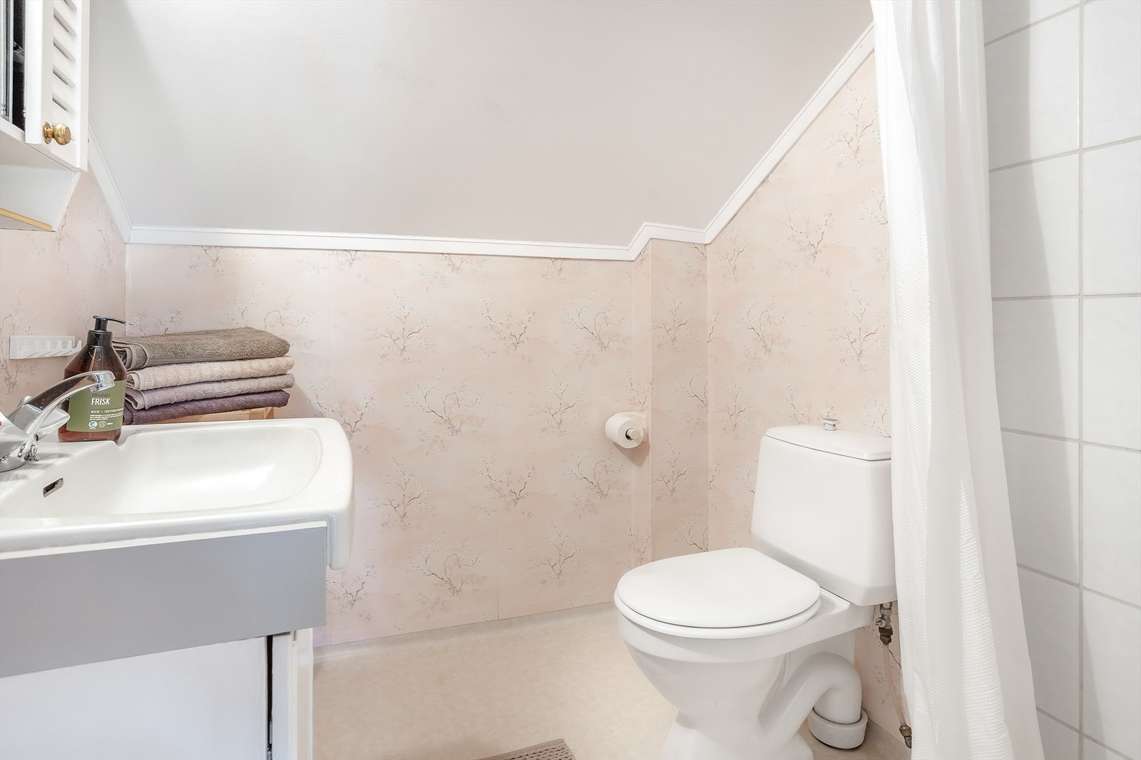 Badet i loftsetasjen har vinylbelegg på gulvet, og en kombinasjon av tapet og flis på veggene. Galleribilde