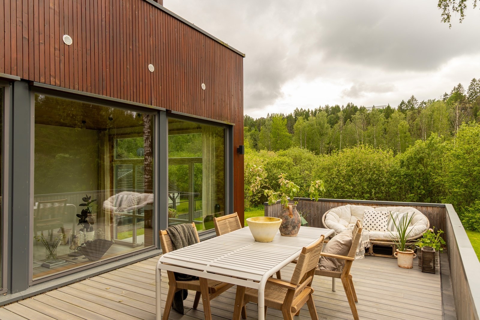 Terrassen utenfor kjøkkenet har en sosial og praktisk beliggenhet, med god kontakt til både stuen og hagen. Boligen er kledd med sibirsk lerk, et eksklusivt og slitesterkt naturmateriale kjent for sin lange levetid. Fargen skyldes behandling med beis. Galleribilde