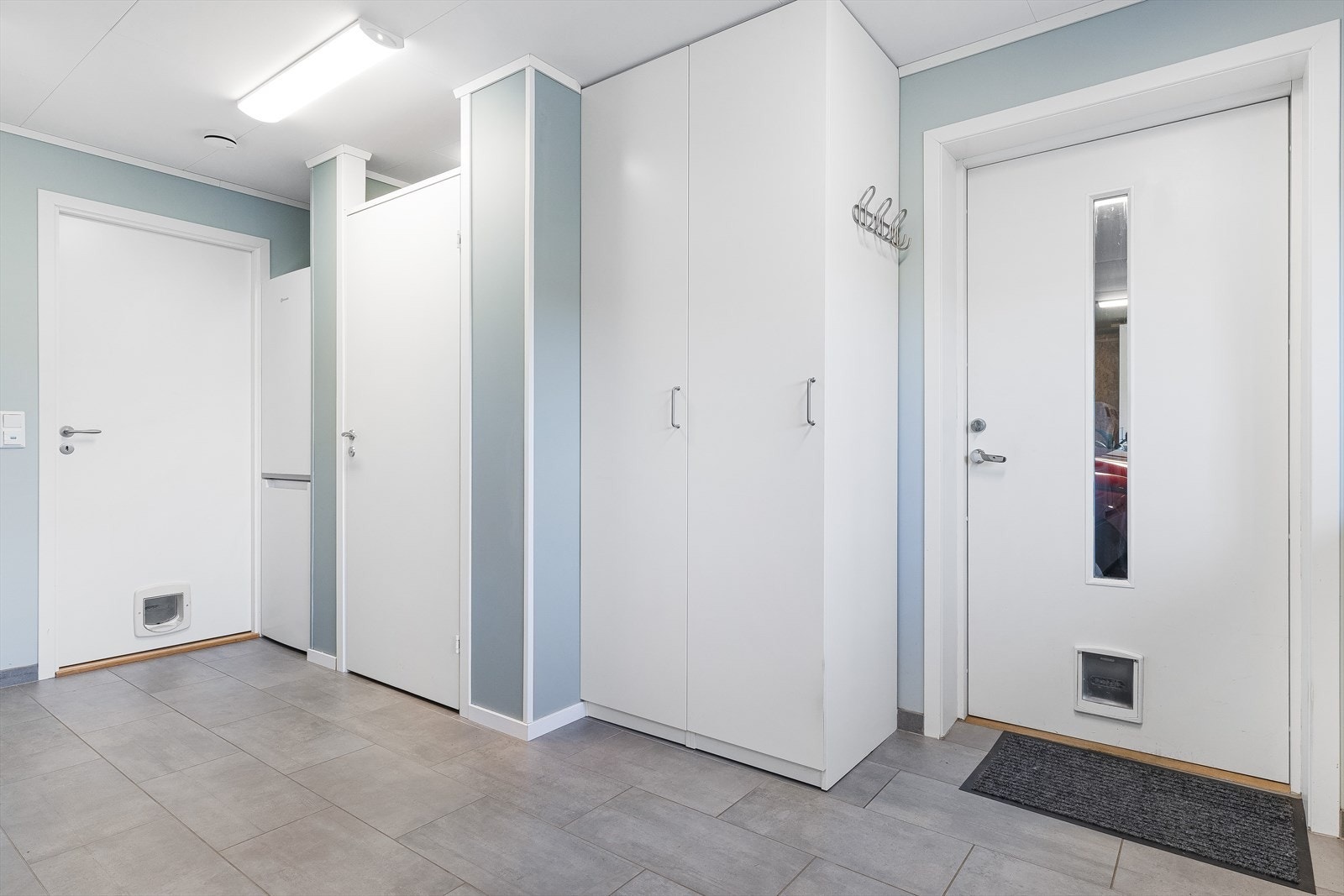Praktisk vaskerom/bakgang med flislagt gulv, veggmontert toalett og opplegg for vaskemaskin. Galleribilde