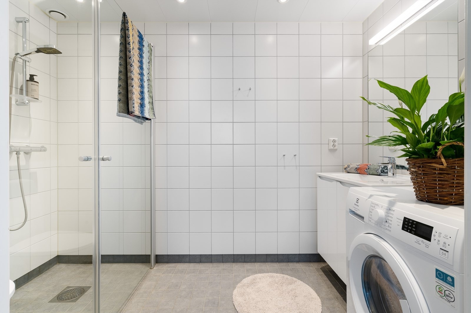 Badet er innredet med dusjhjørne med glassdører, vegghengt toalett, servant med underskap, stort speil med belysning samt opplegg for vaskemaskin. Galleribilde