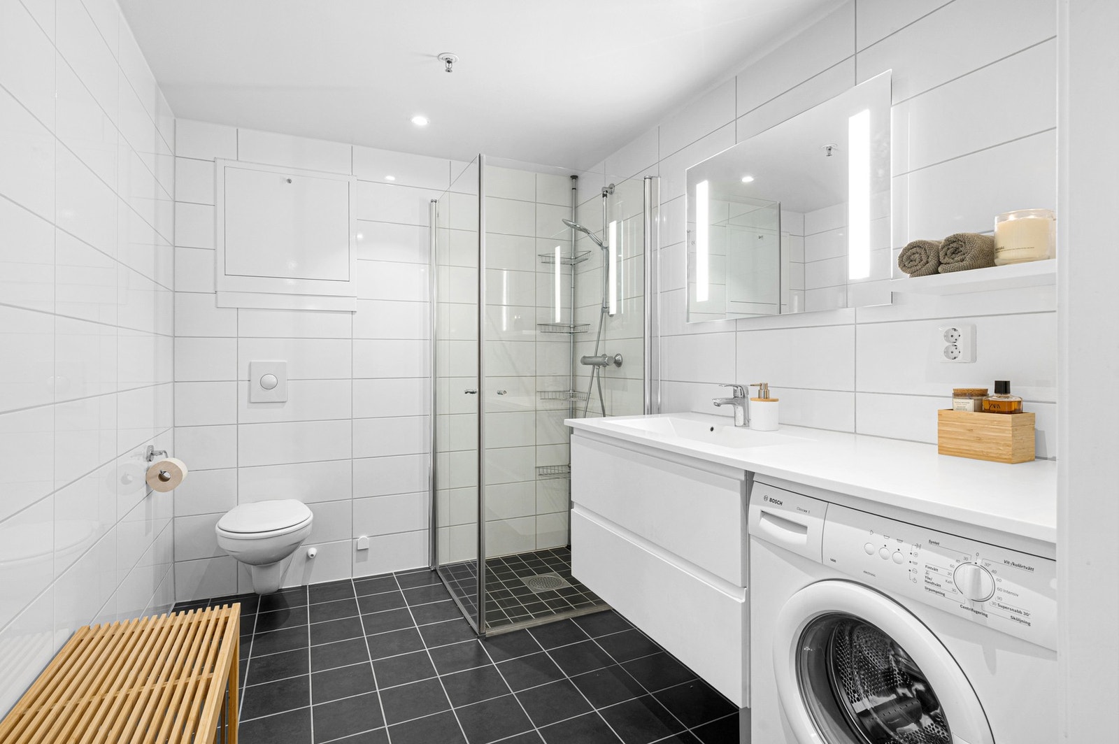 Tidløst og pent flislagt bad på 5,5 kvm. Badet er utstyrt med varmekabler i gulv, vegghengt toalett og innfellbare dusjdører i glass. Galleribilde