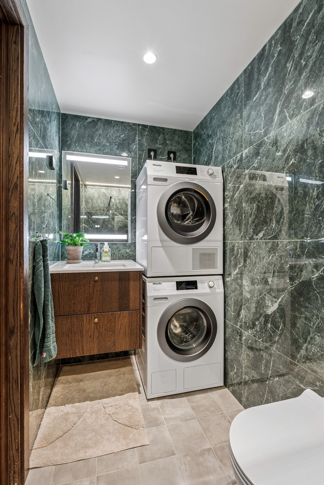 Det andre badet har fliser på vegger og gulv med gulvvarme. Badet har baderomsmøbel fra Strai med servant, benkeplate fra Silestone, dusjnisje, vegghengt toalett og opplegg til vaskemaskin. Galleribilde