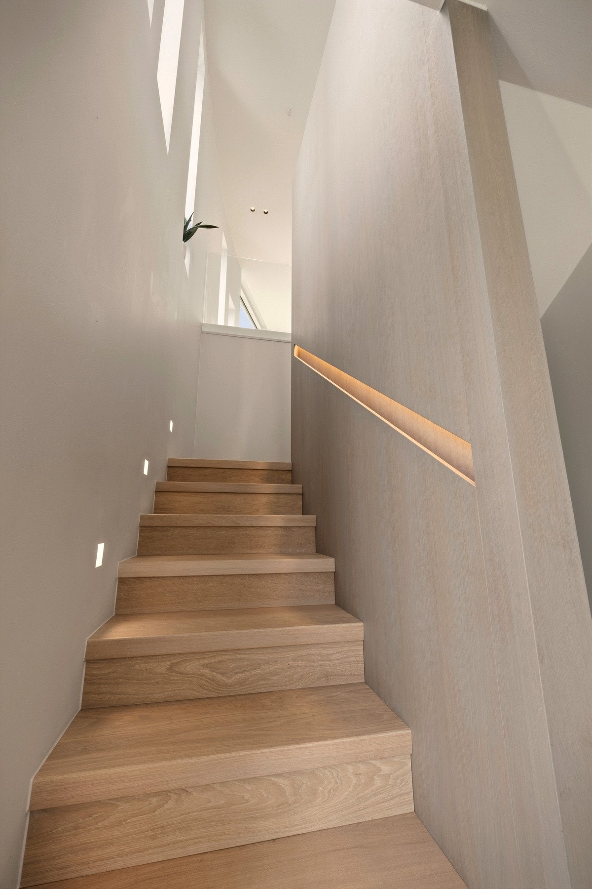 Trappeløpet er utført med gjennomførte materialvalg i eik og ask, og fremstår som en naturlig del av boligens arkitektur. Integrert, indirekte belysning i håndløperen skaper en varm atmosfære og understreker de rene linjene i utformingen. Galleribilde
