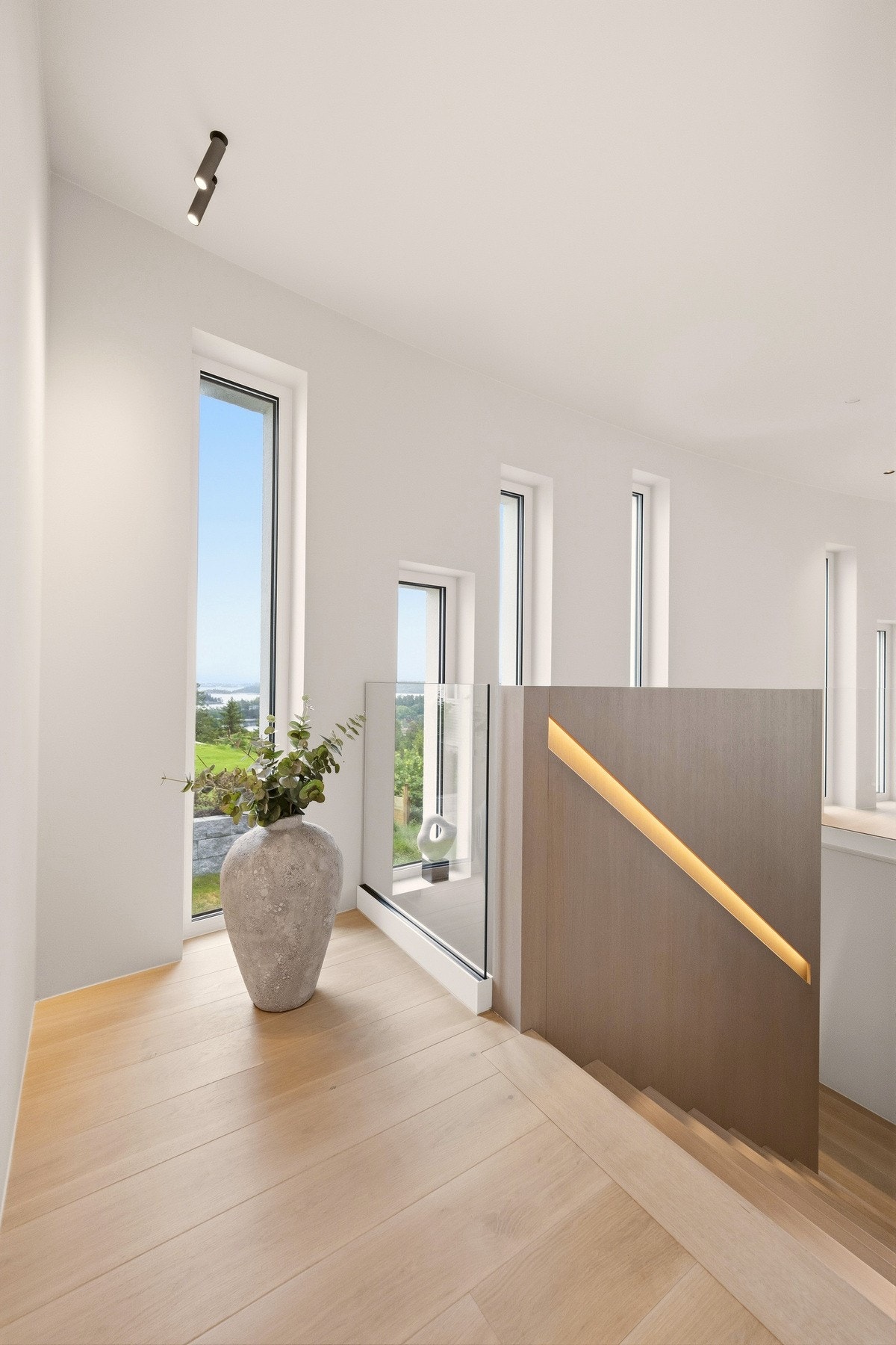 Trappegangen er preget av smale, vertikale vinduer plassert i en gjennomtenkt rytme langs den buede veggen. Sammen med integrert belysning skaper dette et elegant lysspill og understreker boligens arkitektoniske særpreg. Galleribilde