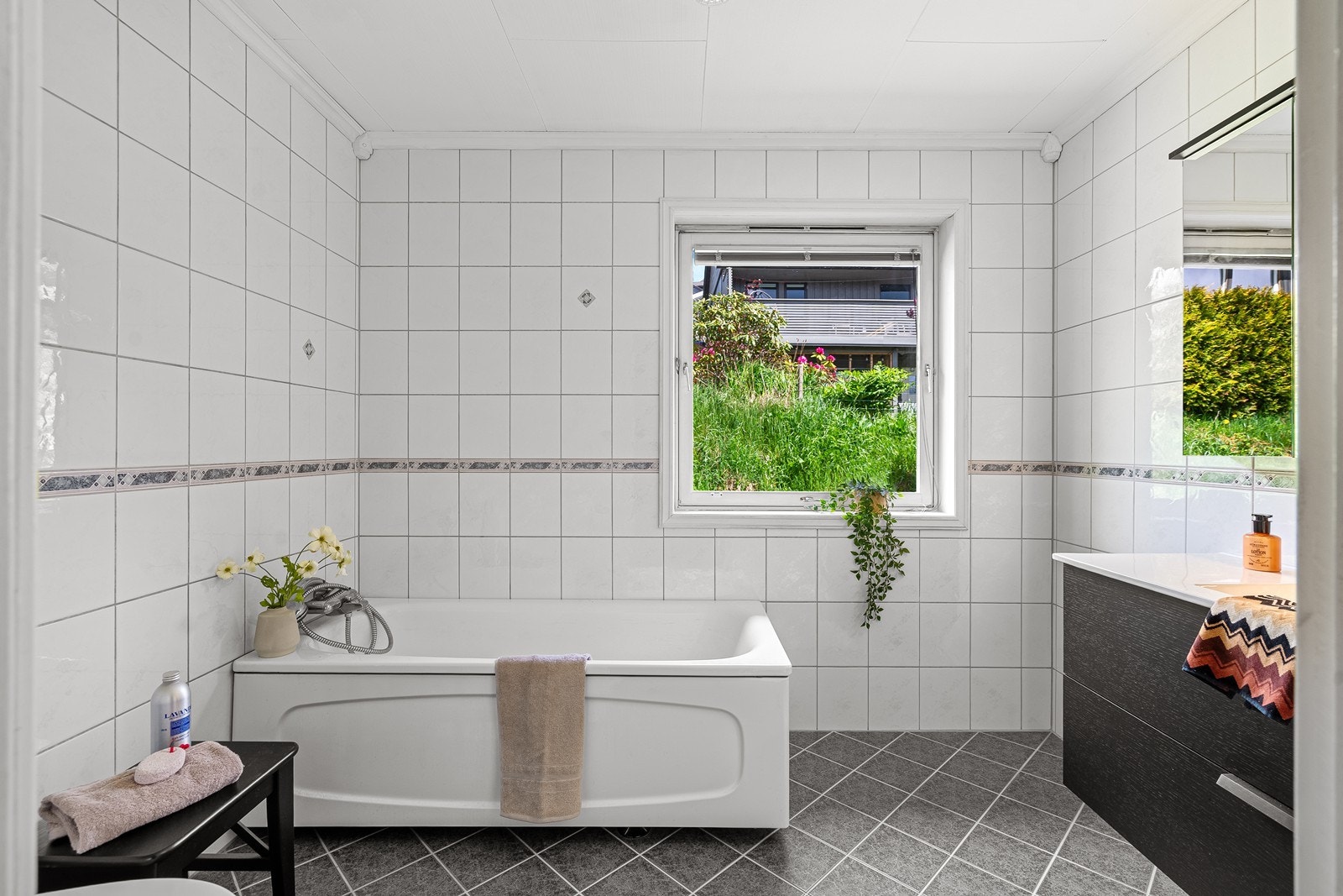 Badet er innredet med toalett, badekar og en praktisk servantinnredning med nedfelt vask i skuffeseksjon, samt stort speilskap. Galleribilde