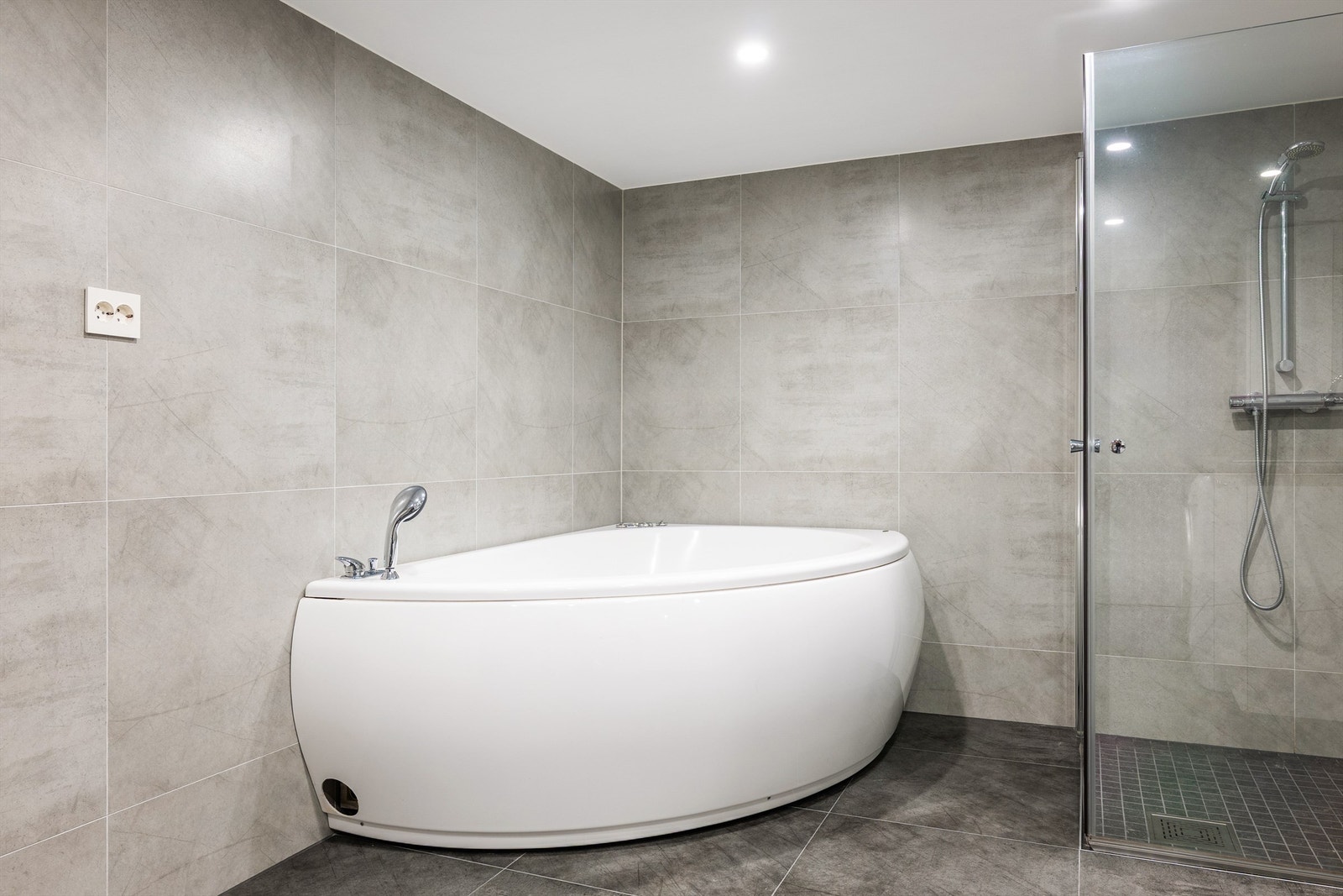 Storformat fliser på vegger og gulv utenfor dusjsonen gir badet helhet. I gulvet er det varme. Galleribilde