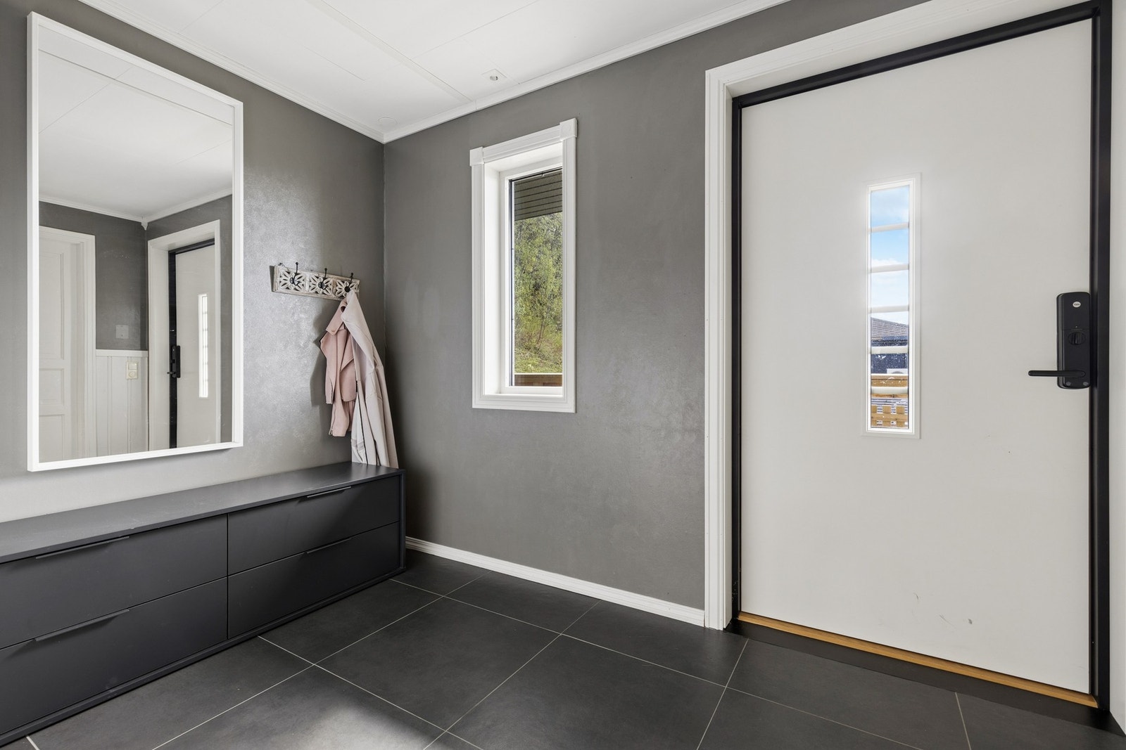 Malt hovedytterdør i tre ønsker velkommen inn i en romslig entré. Galleribilde