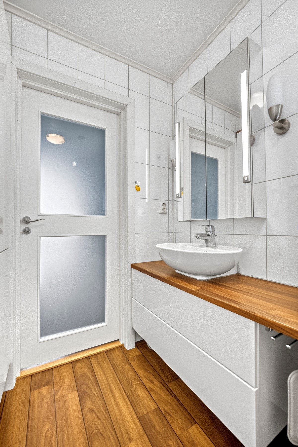 Badet har gulvbelegg i parkettmønster, flisplater på veggene og gulvvarme. Galleribilde