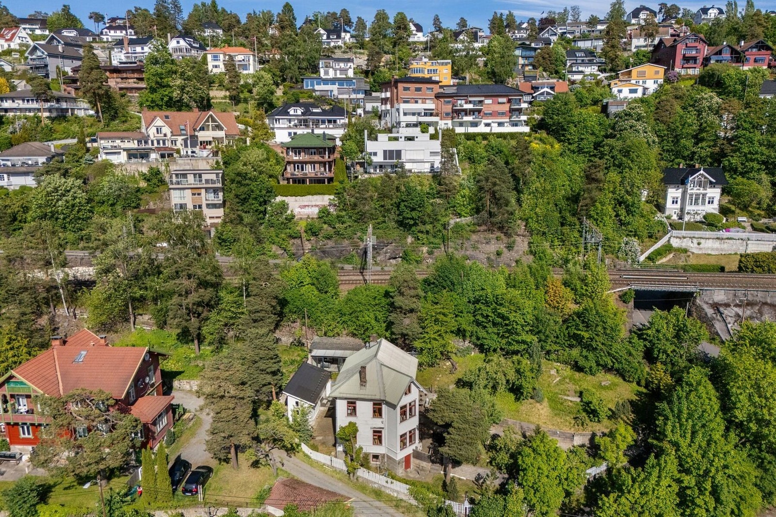 Dronebildet fremhever eiendommens romslige tomt og de mange hyggelige uteområdene som omkranser boligen. Galleribilde
