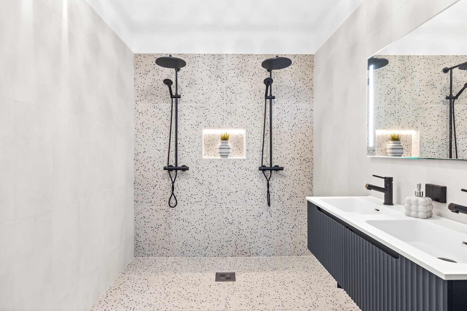 Badet i 1. etasje har et stramt og stilig uttrykk med flislagte overflater, behagelig gulvvarme og skyhøy takhøyde. Galleribilde