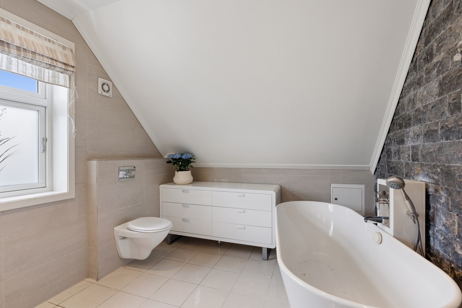 Badet er utstyrt med badekar som må repareres eller skiftes, og en fondvegg med steinpanel gir en stilig kontrast. Galleribilde