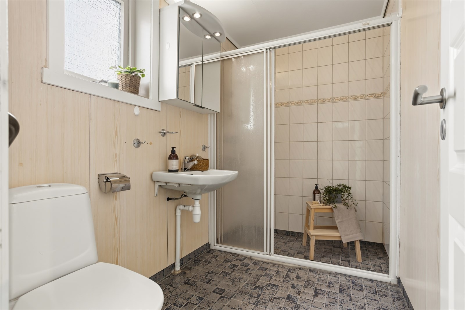 Badet i sokkelleiligheten har flislagt gulv med varmekabler. Badet er bygget på 90-tallet og har generelt behov for oppgradering. Galleribilde