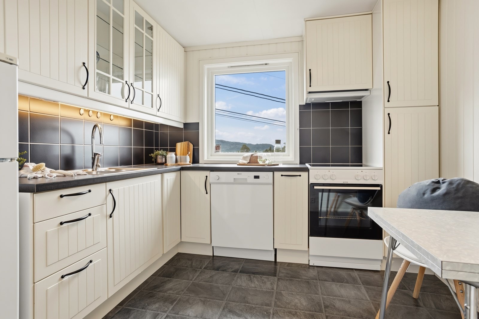 Kjøkkeninnredning fra Ikea i sokkelleiligheten, med profilerte hvite fronter, laminat benkeplate og fliser over benken. Galleribilde