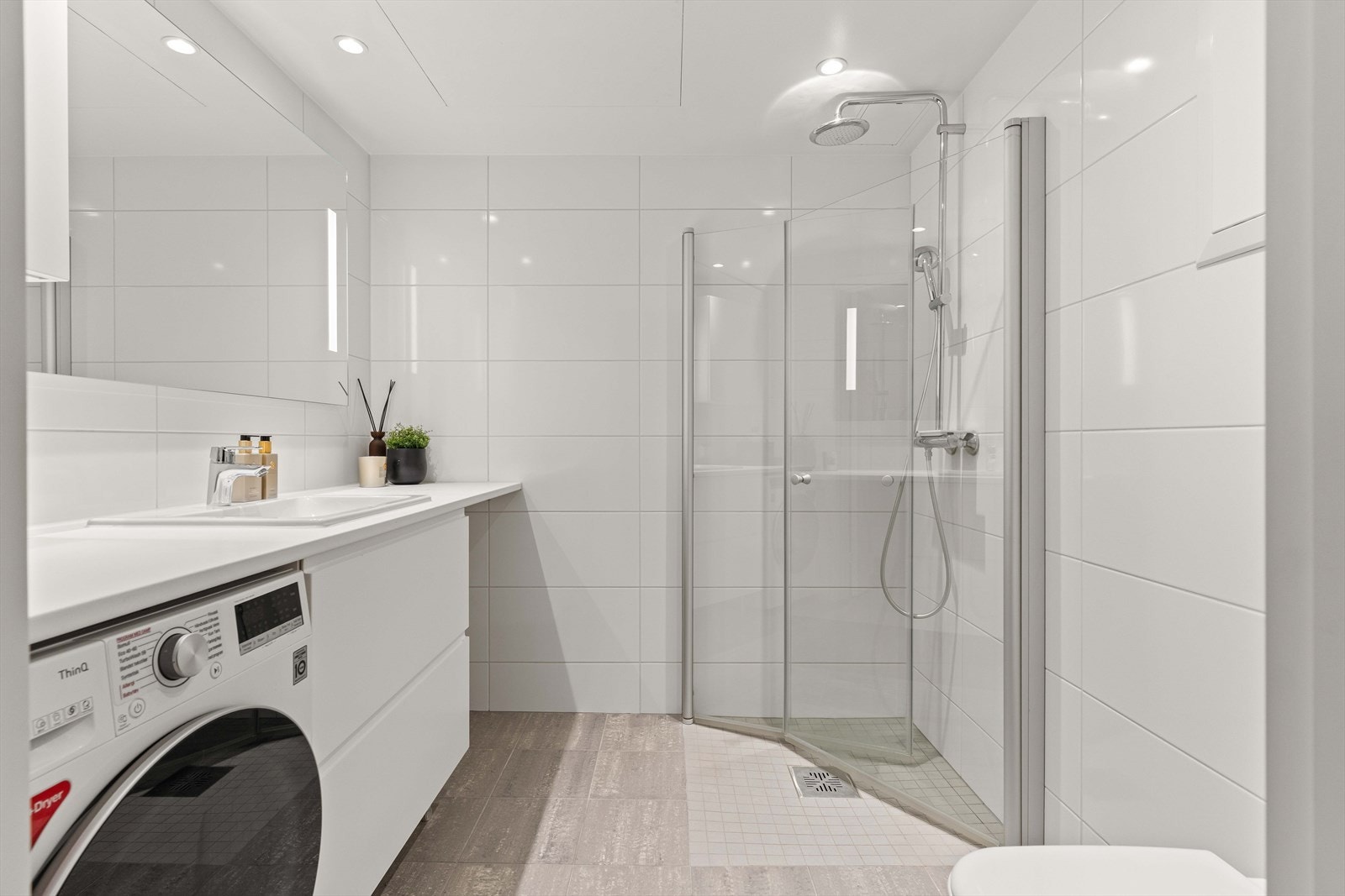 Delikat bad med moderne fliser, dusjhjørne og praktisk opplegg for vaskemaskin. Badet fremstår tidsriktig og lettstelt, med god plass til daglige rutiner. Galleribilde