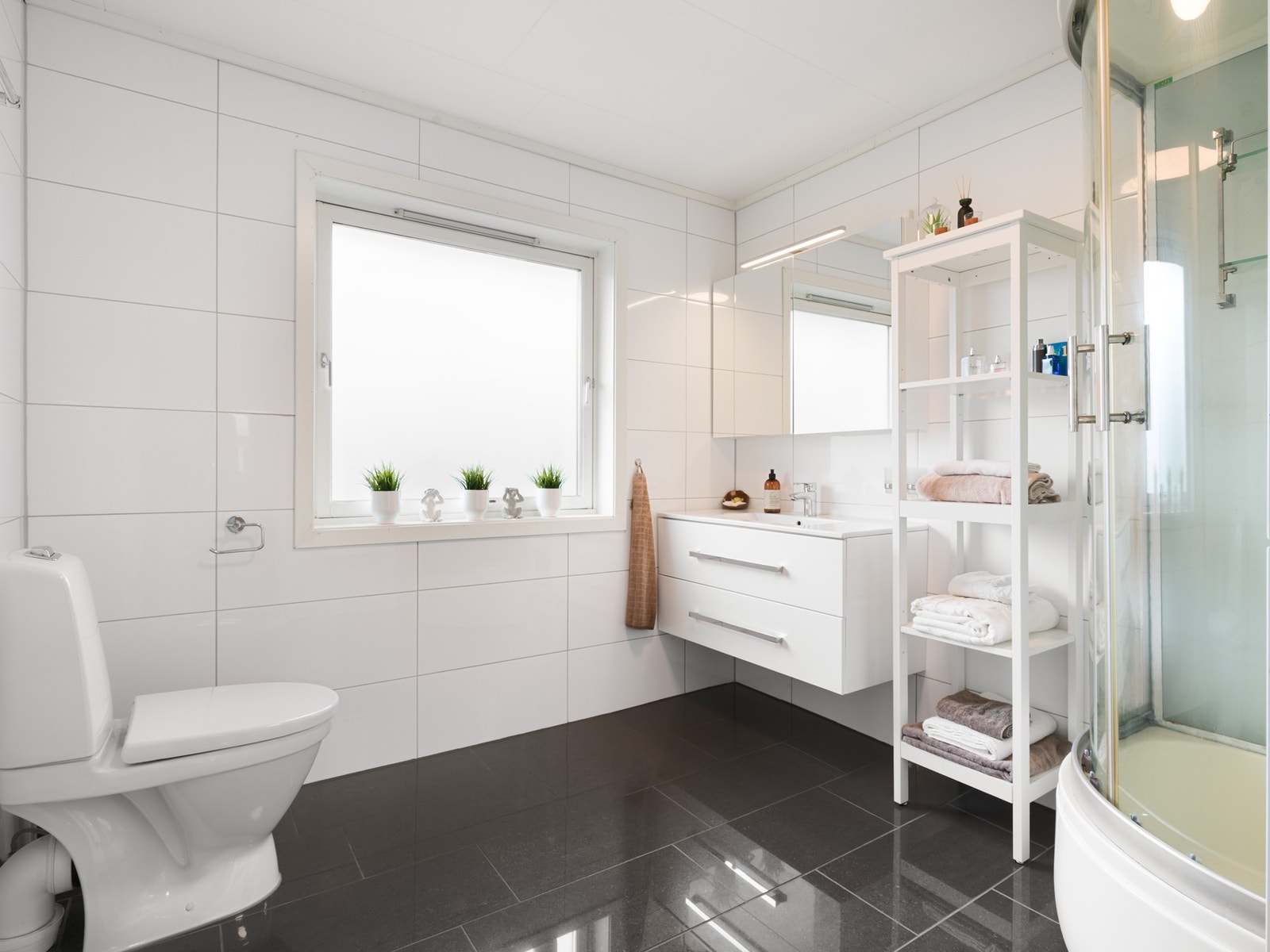 Badet i første etasje har fliser på gulv og vegger, samt varmekabler i gulv. Badet er innredet med servantskap, høyskap og speilskap. Videre er rommet utstyrt med toalett og dusjkabinett. Galleribilde