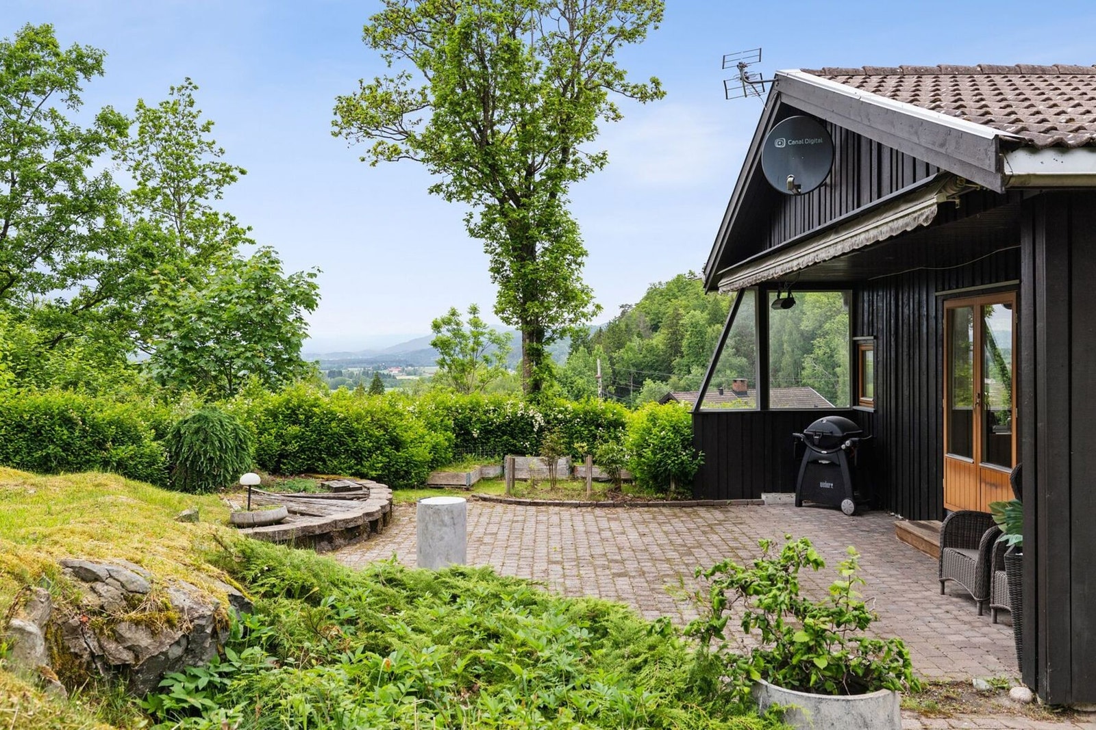 Fasadebilde av vestlig side av huset. Her er det også en stor steinsatt uteplass og takoverbygg/marklise. Galleribilde