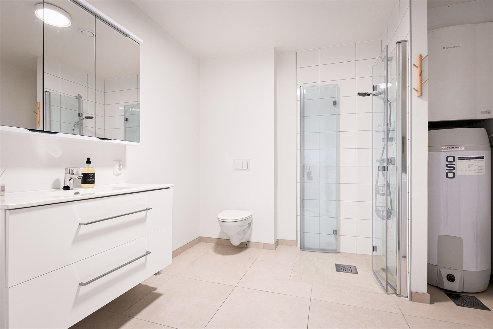 Videre er det vegghengt toalett, dusjhjørne og opplegg for vaskemaskin og tørketrommel. Badet har en praktisk planløsning og gode oppbevaringsmuligheter. Galleribilde
