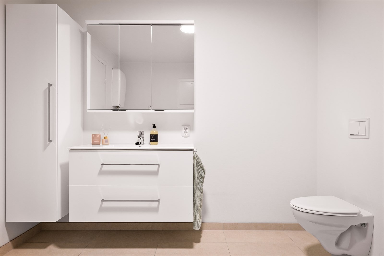 Badet er innredet med en stilren servant med skuffer under, speilskap med integrert belysning, og tilhørende høyskap. Galleribilde