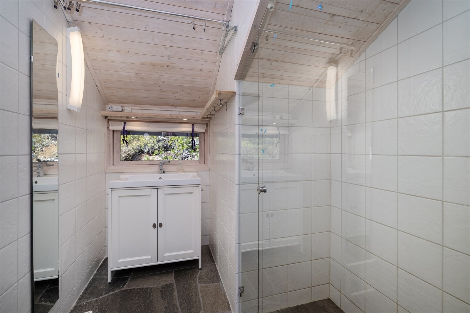 Badet har skifer på gulvet, flislagte vegger og et dusjavlukke bygget opp av fastmonterte glassfelt. Gulvvarme. Galleribilde